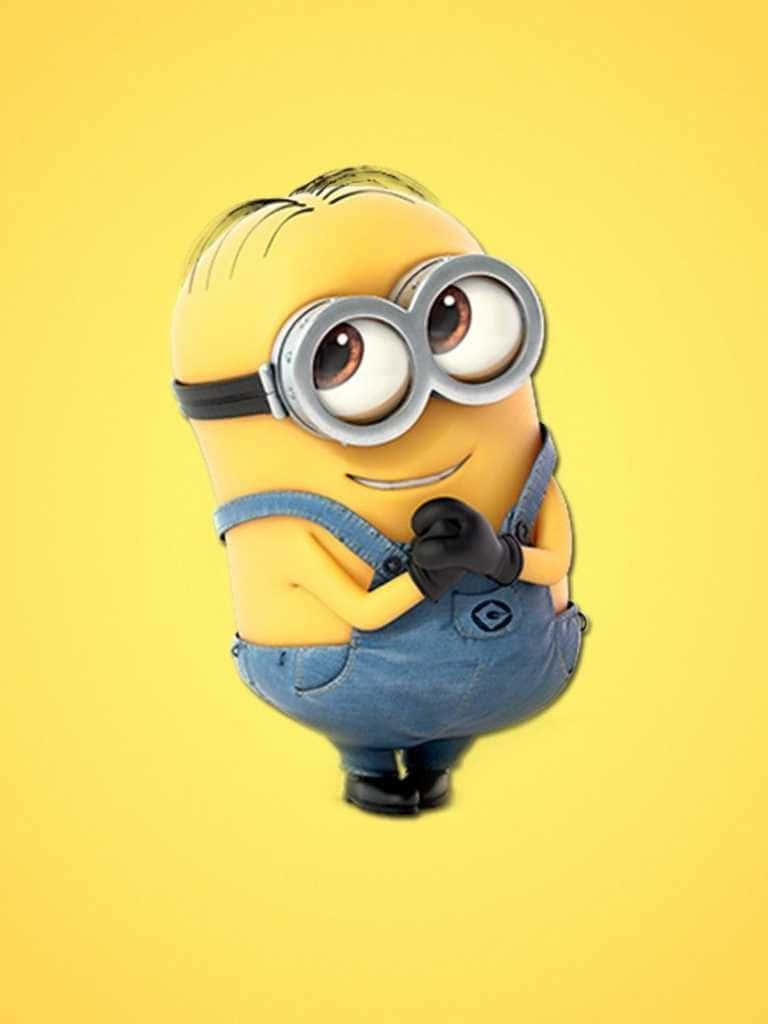 Minion 桌布 壁紙 — 一個穿著藍色工裝褲和護目鏡的開心黃色小小兵，在明亮的黃色背景前擺出自信的姿勢。