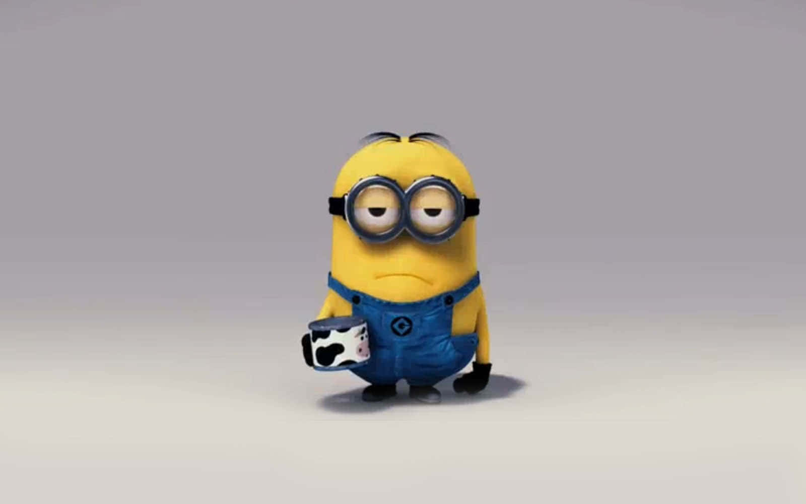 Despicable 桌布 壁紙 — 一個穿著藍色工裝褲的黃色Minion，在純灰色背景前拿著一個牛紋馬克杯。