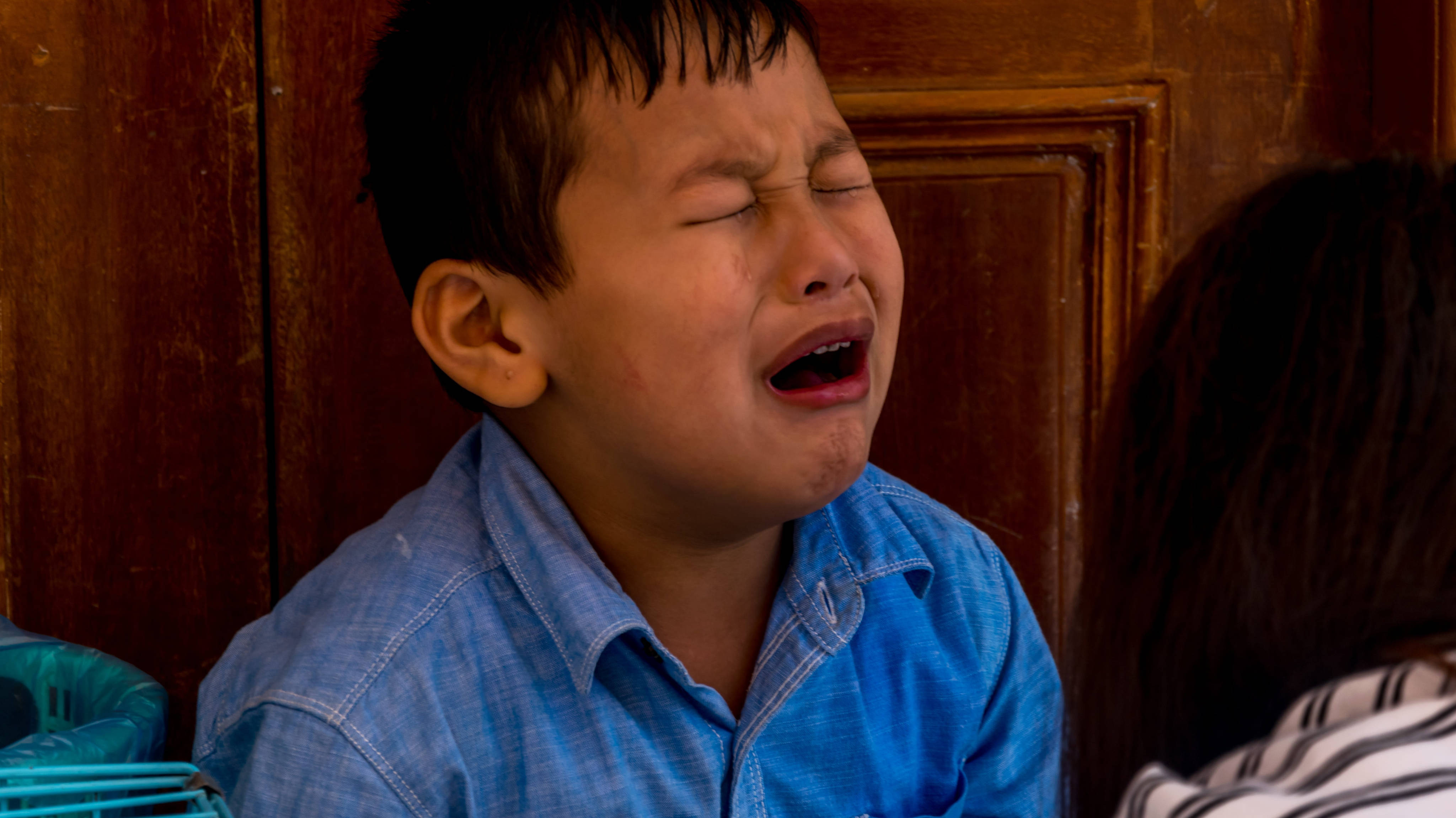 crying sad boy 桌布 壁紙 — 一個穿著藍色襯衫的小男孩，在木門背景下緊閉雙眼大聲哭泣。