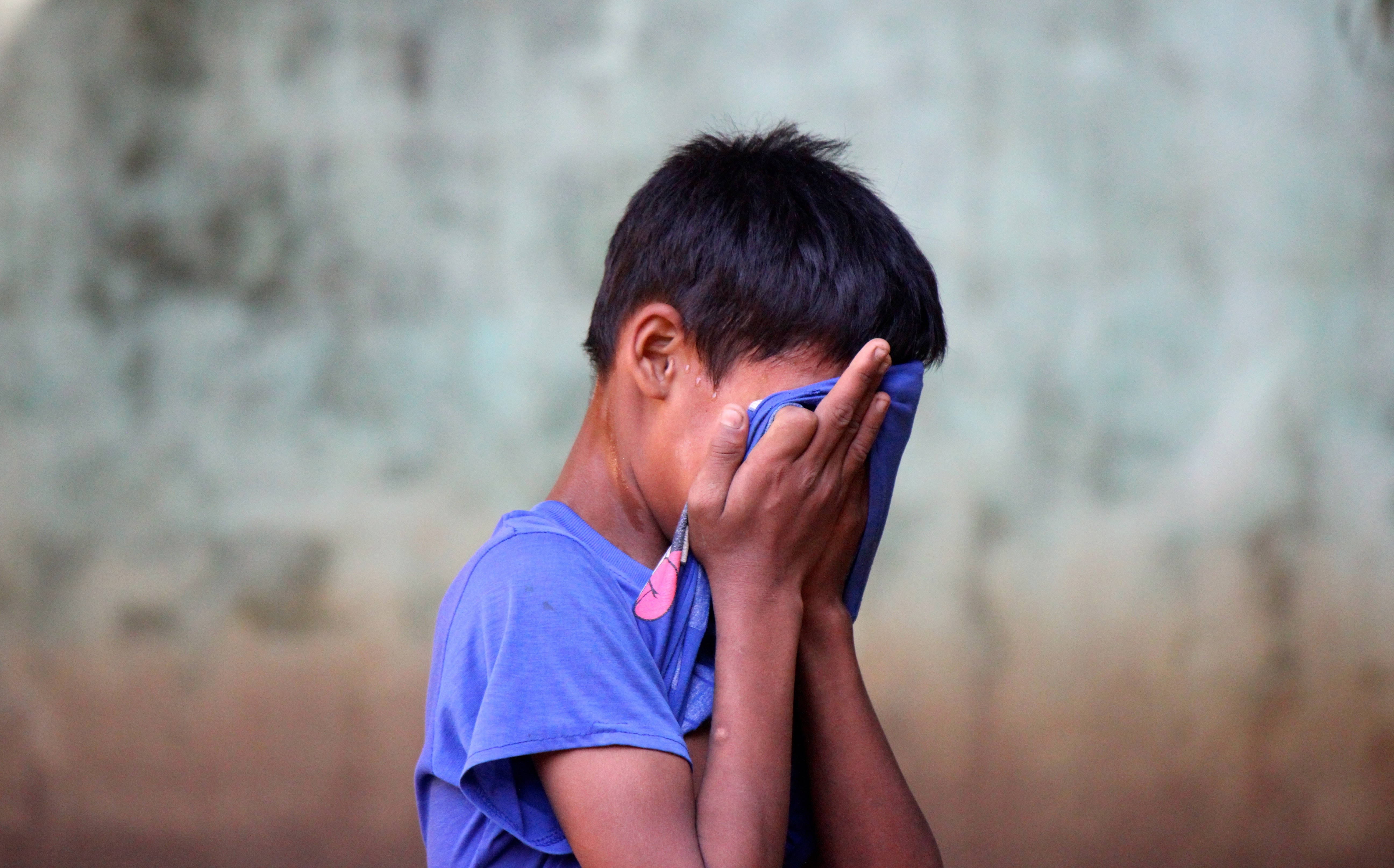 crying sad boy 桌布 壁紙 — 一個穿著藍色襯衫的小男孩，用雙手遮住臉，靠在一面風化的牆上。