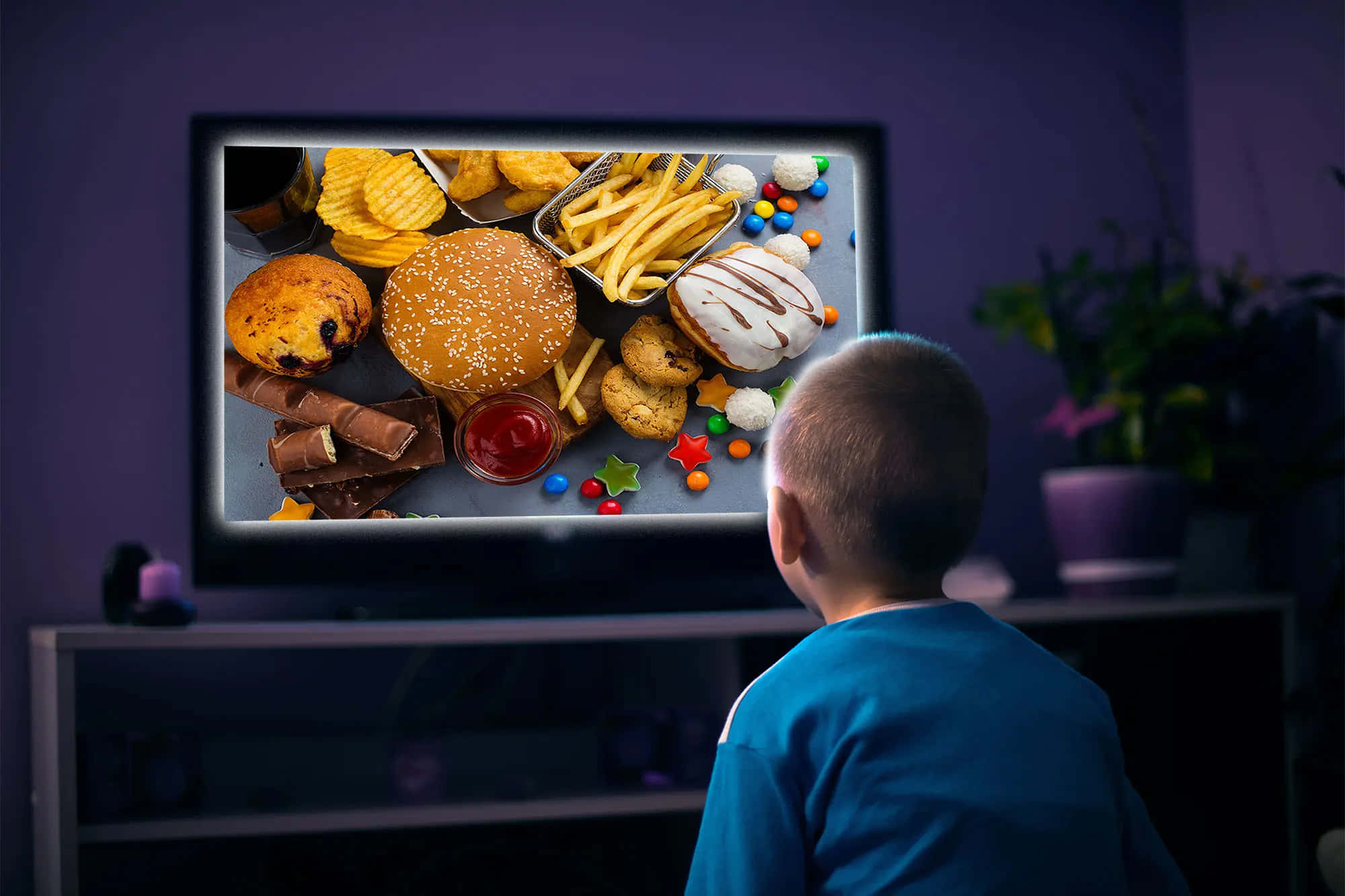 watching tv 桌布 壁紙 — 一個穿著藍色襯衫的小男孩在燈光昏暗的紫色房間裡，看著充滿色彩繽紛垃圾食物（如漢堡、薯條和糖果）的電視螢幕。
