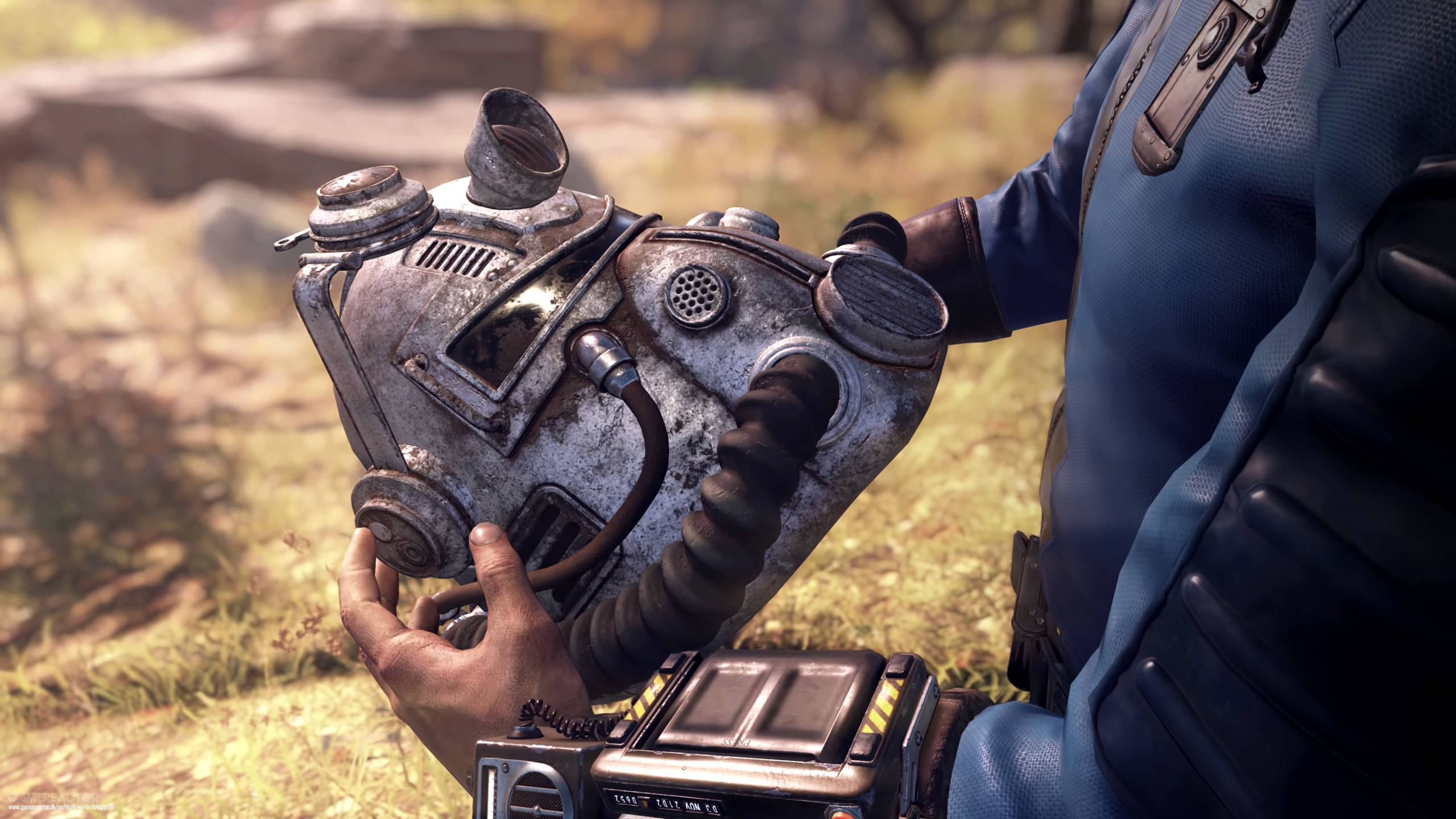 Fallout 76 桌布 壁紙 — 一個穿著藍色西裝的角色，在陽光明媚的草地上拿著一個帶有軟管和通風口的破舊金屬防毒面具。