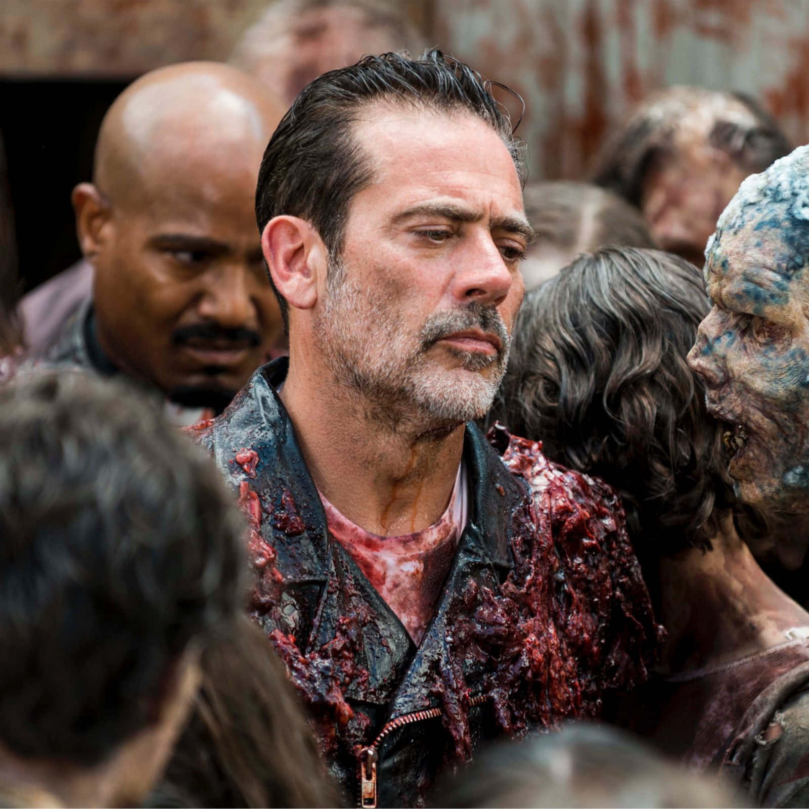 walking dead 桌布 壁紙 — 一個穿著血跡斑斑皮夾克的男人，站在一群怪誕的殭屍之中，場景陰森恐怖。