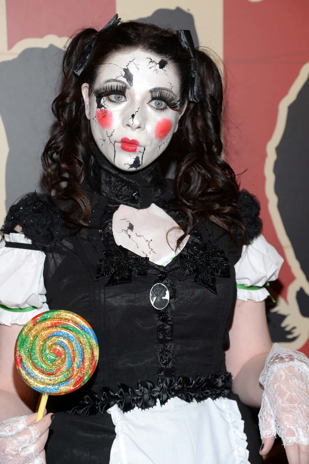Halloween Face Paint 桌布 壁紙 — 一個穿著裂面小丑服裝的人，在風格化的紅色和灰色背景下拿著彩虹棒棒糖。