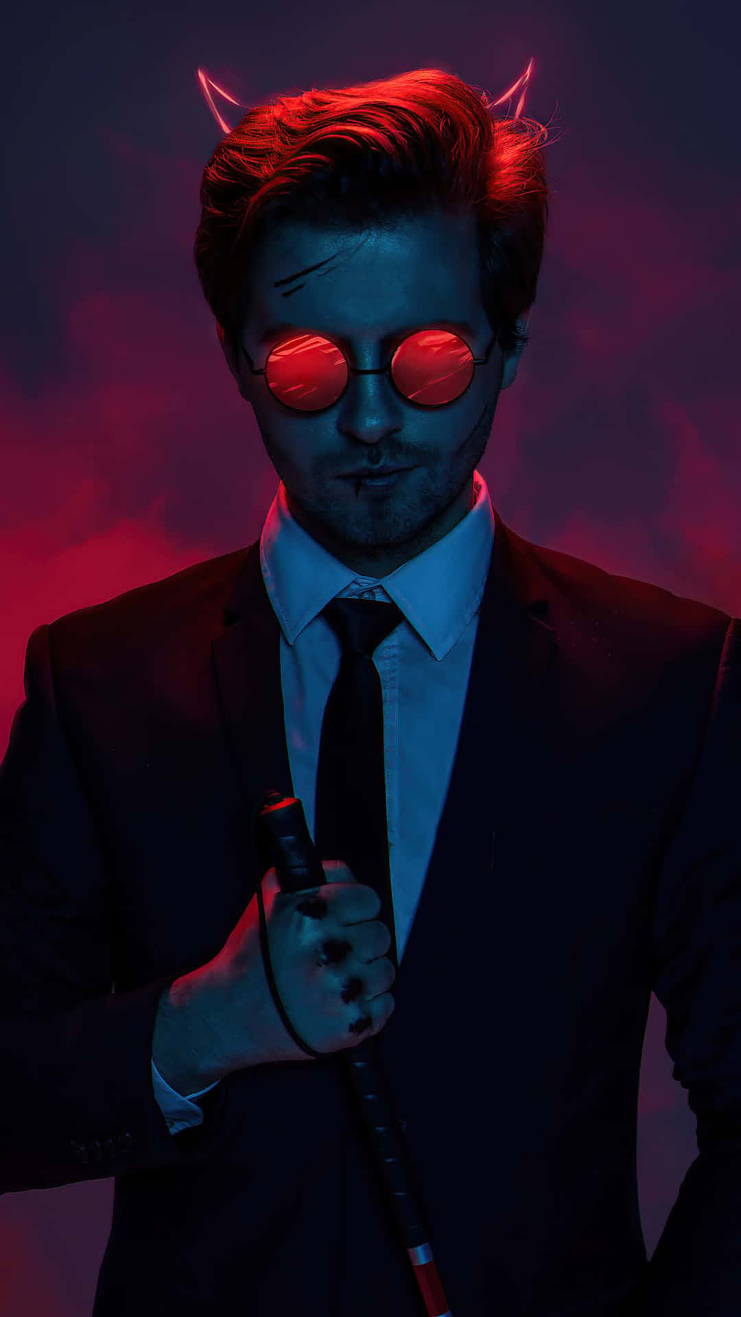 惡魔 桌布 壁紙 — 一個穿著西裝、戴著惡魔角和紅色太陽眼鏡的男人，在煙霧瀰漫的紅藍背景下拿著手杖。