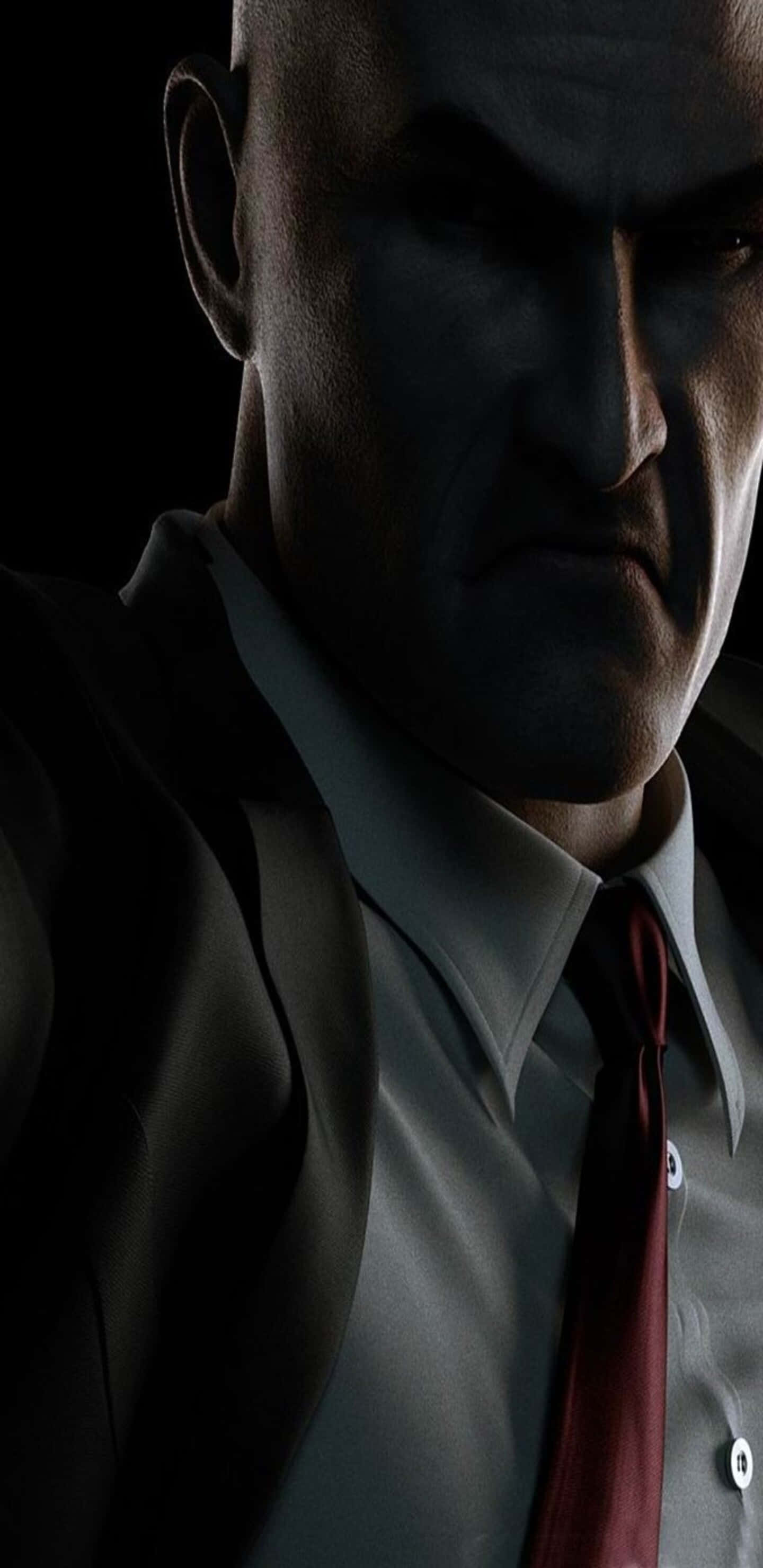 Pixel 3xl Hitman 桌布 壁紙 — 一個穿著西裝、打紅色領帶的威嚇光頭男子，在陰暗的黑暗中凝視。