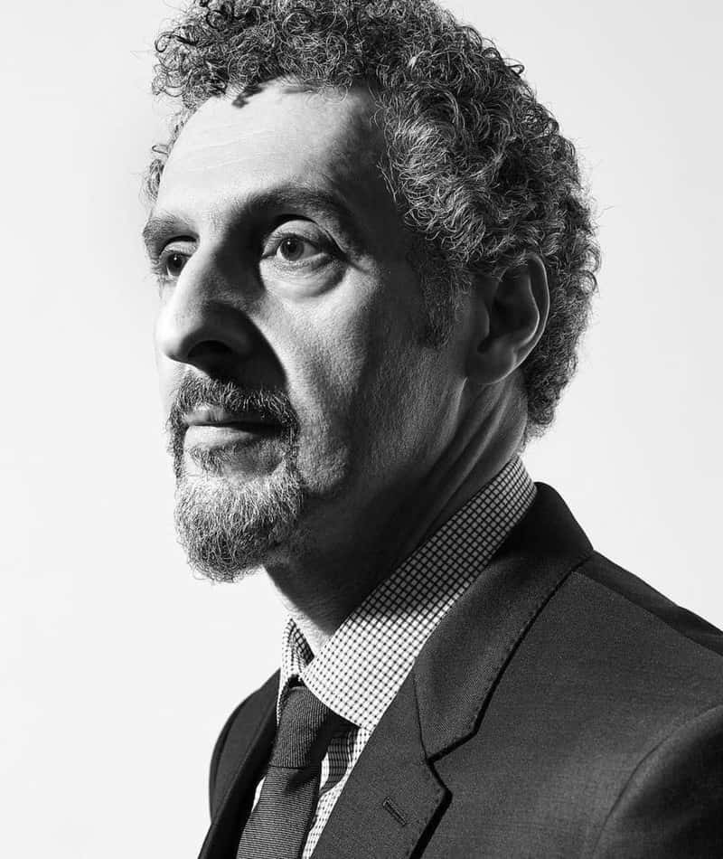 John Turturro 桌布 壁紙 — 一個穿著西裝、留著捲髮和鬍子的男人，若有所思地望向一邊的黑白肖像。