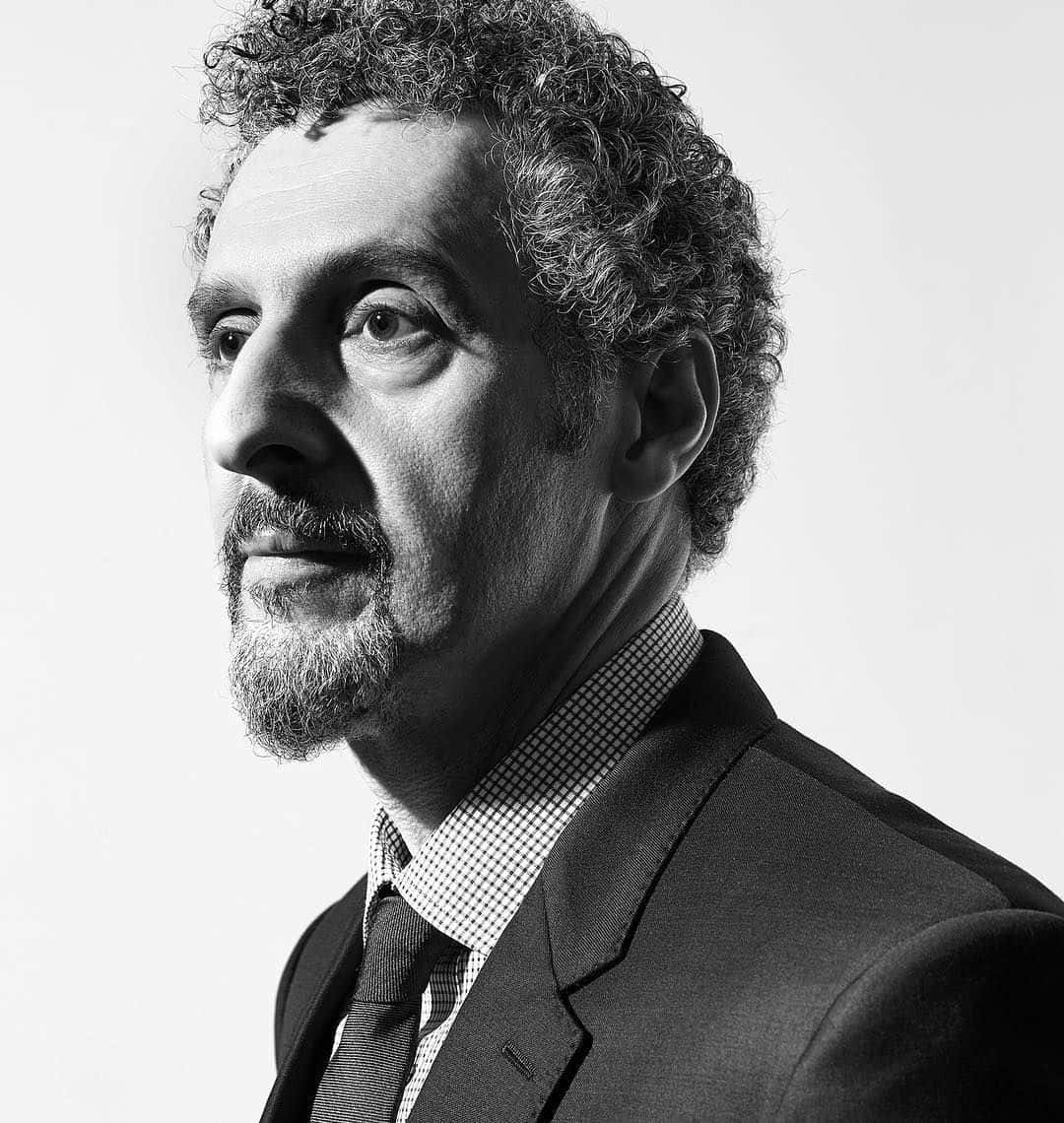John Turturro 桌布 壁紙 — 一個穿著西裝、留著捲髮和鬍子的男人，若有所思地望向一邊的黑白肖像。