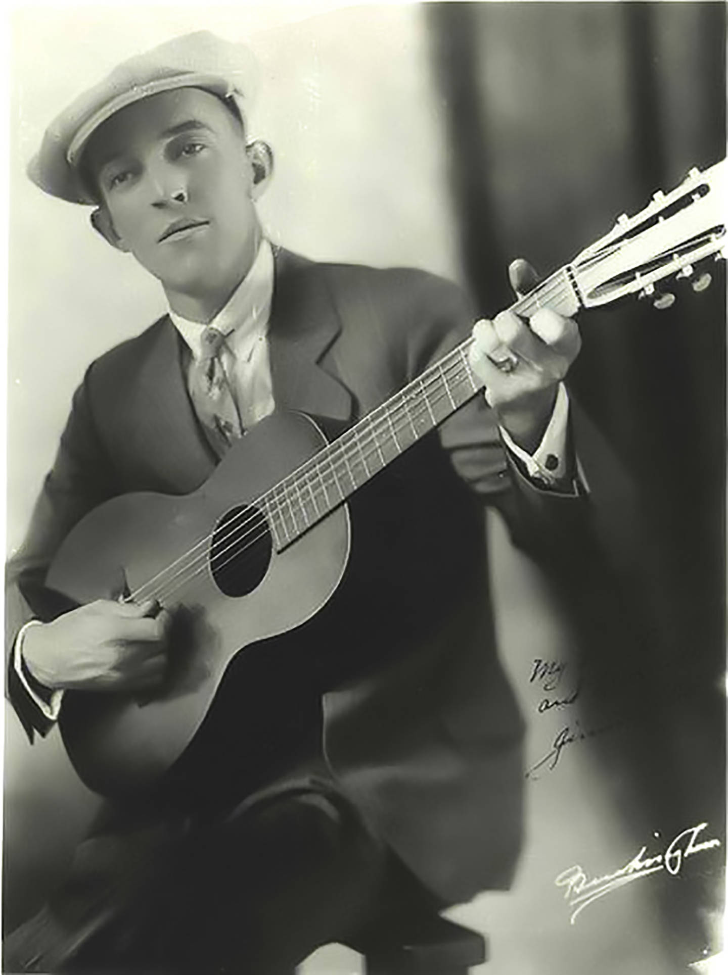 guitar player 桌布 壁紙 — 一個穿著西裝和帽子、手持帶有手寫簽名木吉他的男士的復古黑白肖像。