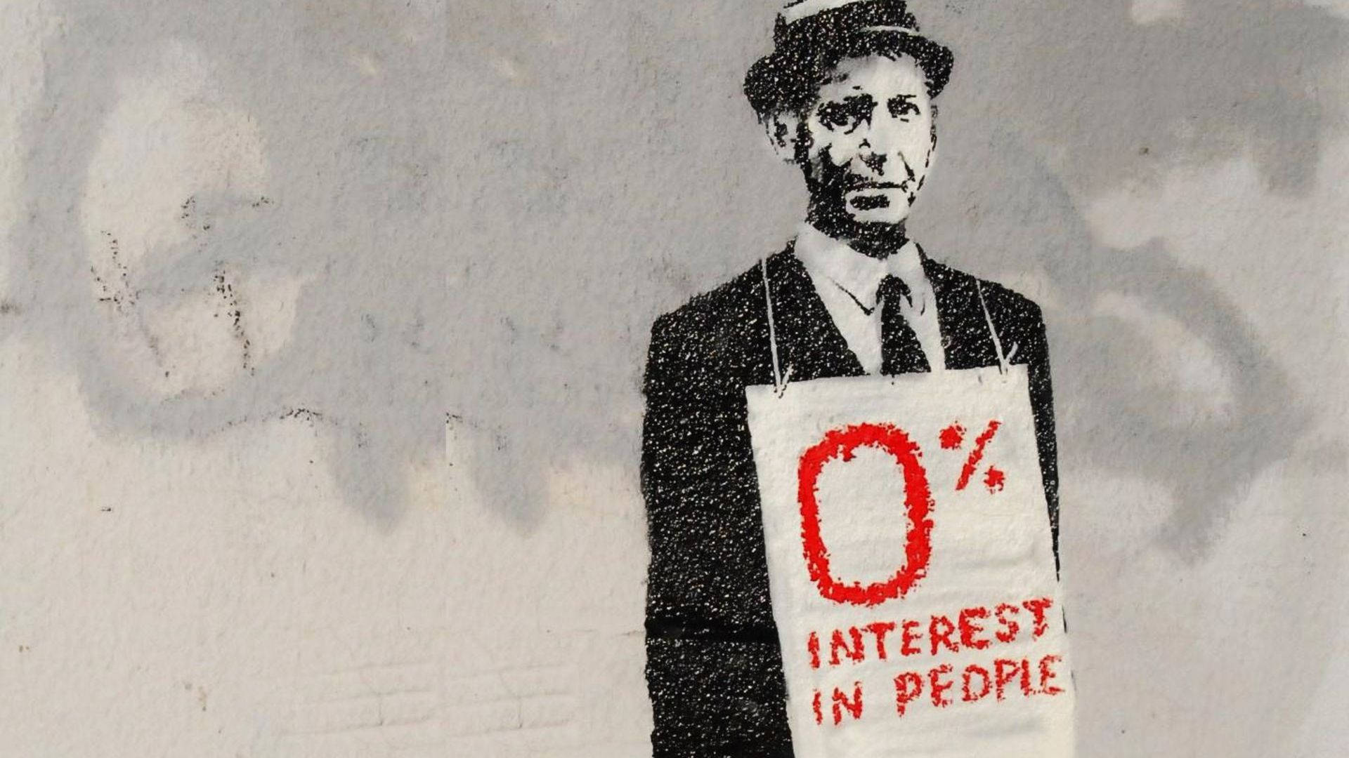 Banksy 桌布 壁紙 — 一個穿著西裝和帽子的男人的粗糙模板塗鴉，拿著一個寫著 0% INTEREST IN PEOPLE 的牌子，背景是風化的牆壁。