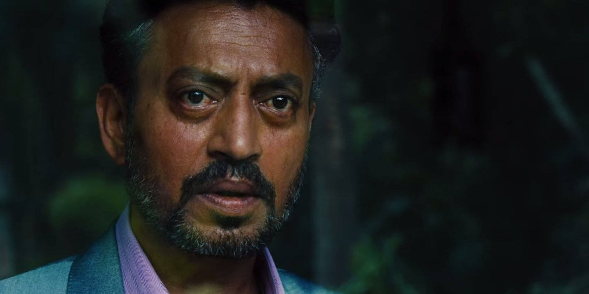 Irrfan Khan 桌布 壁紙 — 一個穿著西裝和紫色襯衫、表情嚴肅的男人特寫，背景是暗色模糊的。