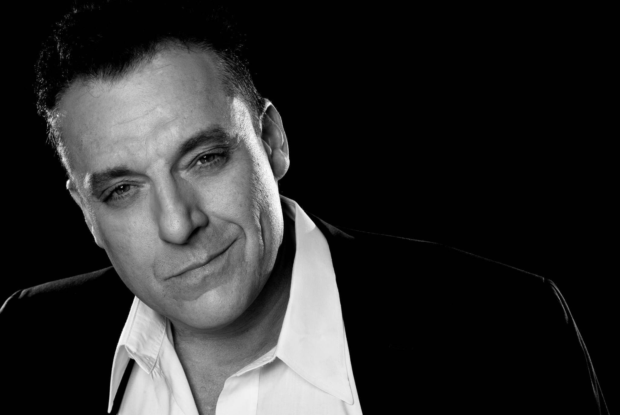 actor 桌布 壁紙 — 一個穿著西裝和襯衫的男人的黑白肖像，背景黑暗，帶著微妙的笑容。