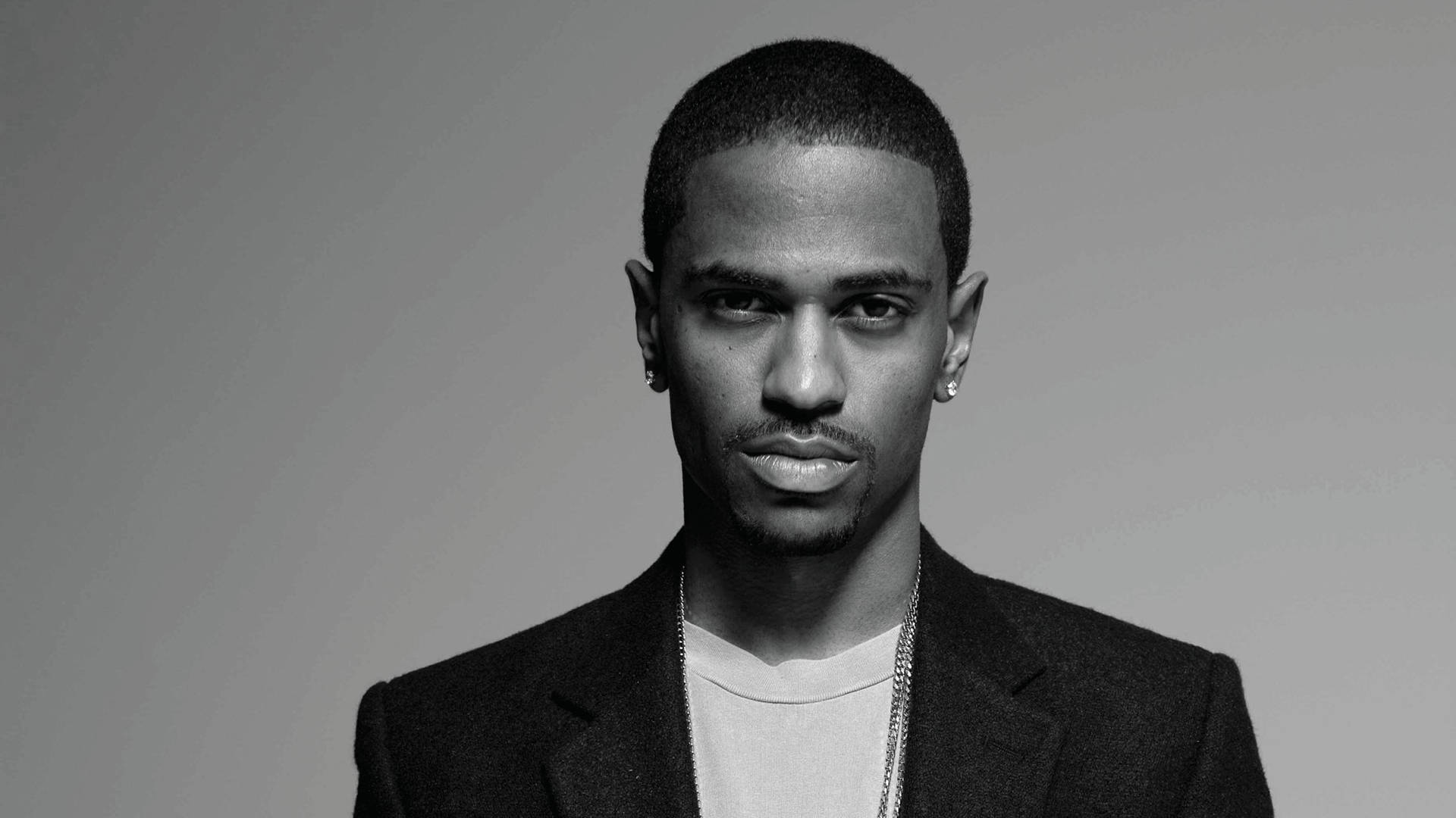 Big Sean 桌布 壁紙 — 一個穿著西裝外套和鏈條項鍊、表情嚴肅的男人的黑白肖像，背景為純灰色。