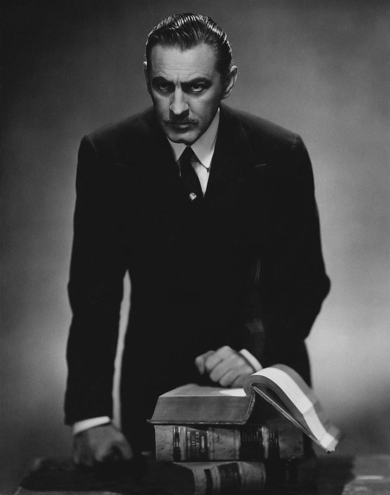 actor 桌布 壁紙 — 一個穿著西裝的嚴肅男子，俯身在一堆書上，表情認真，是一張戲劇性的黑白工作室肖像。