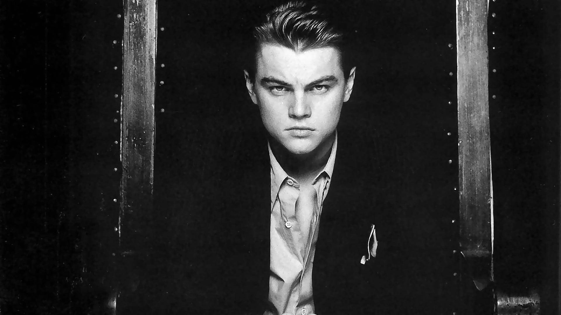 Dicaprio 桌布 壁紙 — 一個穿著西裝的年輕男子透過鉚接金屬欄杆凝視的黑白肖像。