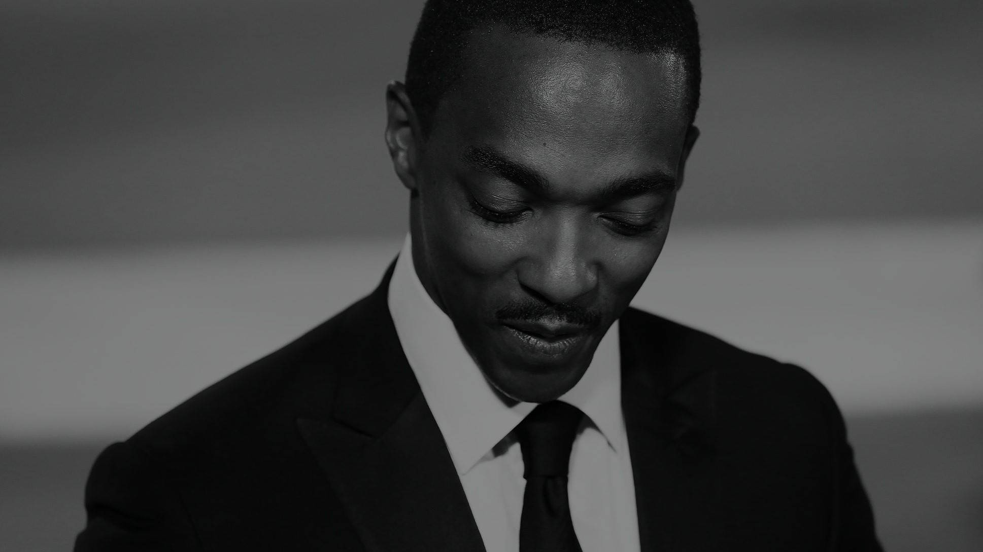 Anthony Mackie 桌布 壁紙 — 一個穿著西裝的男人低頭微笑的黑白特寫。