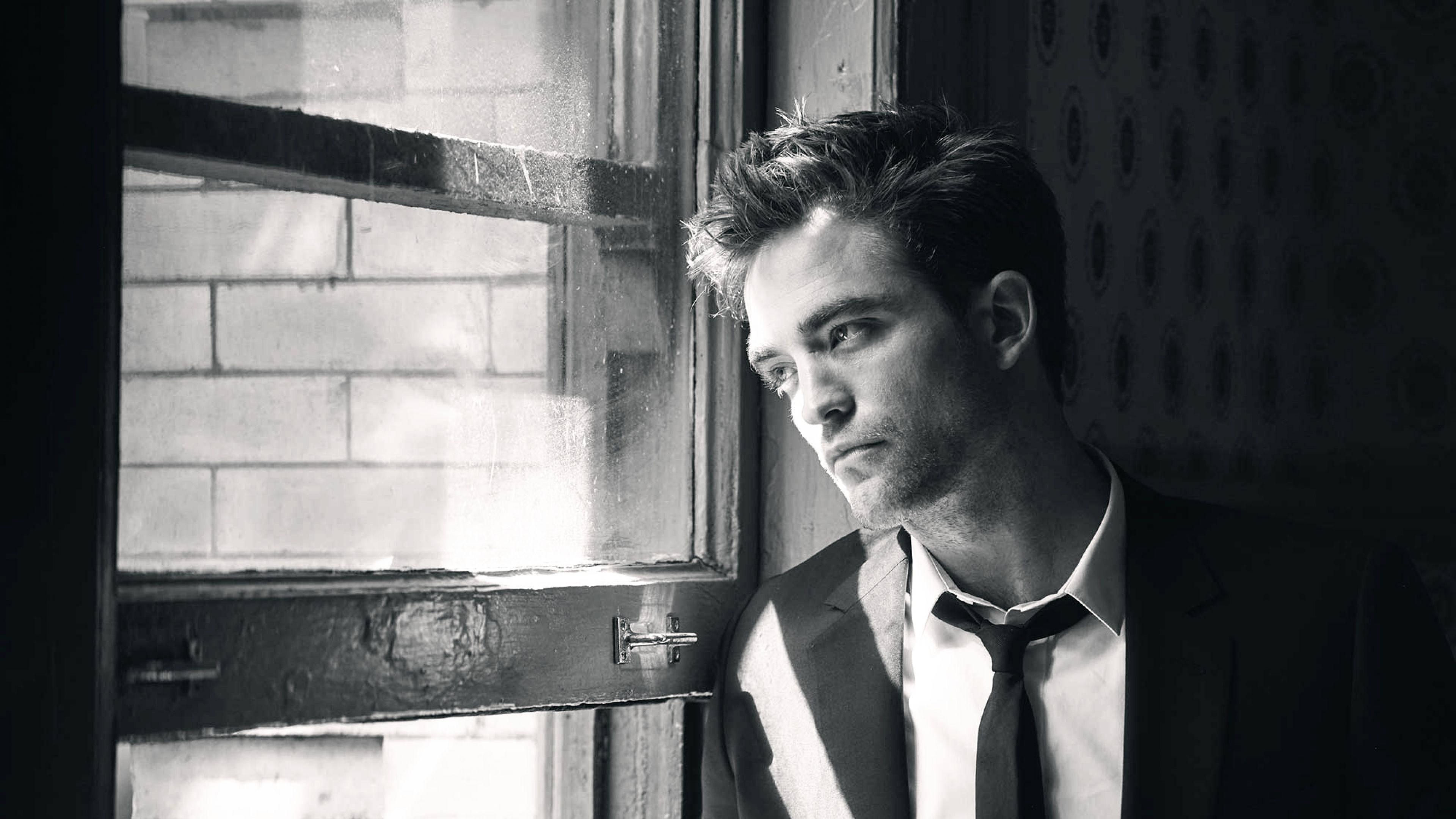Robert Pattinson 桌布 壁紙 — 一個穿著西裝的男人在單色肖像中沉思地靠著風化的窗框。