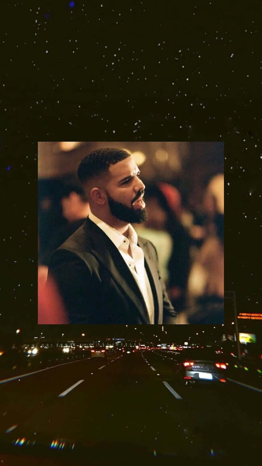 Aesthetic Drake 桌布 壁紙 — 一個穿著西裝的男人在星空和模糊的高速公路與車燈背景下沉思地凝視著。