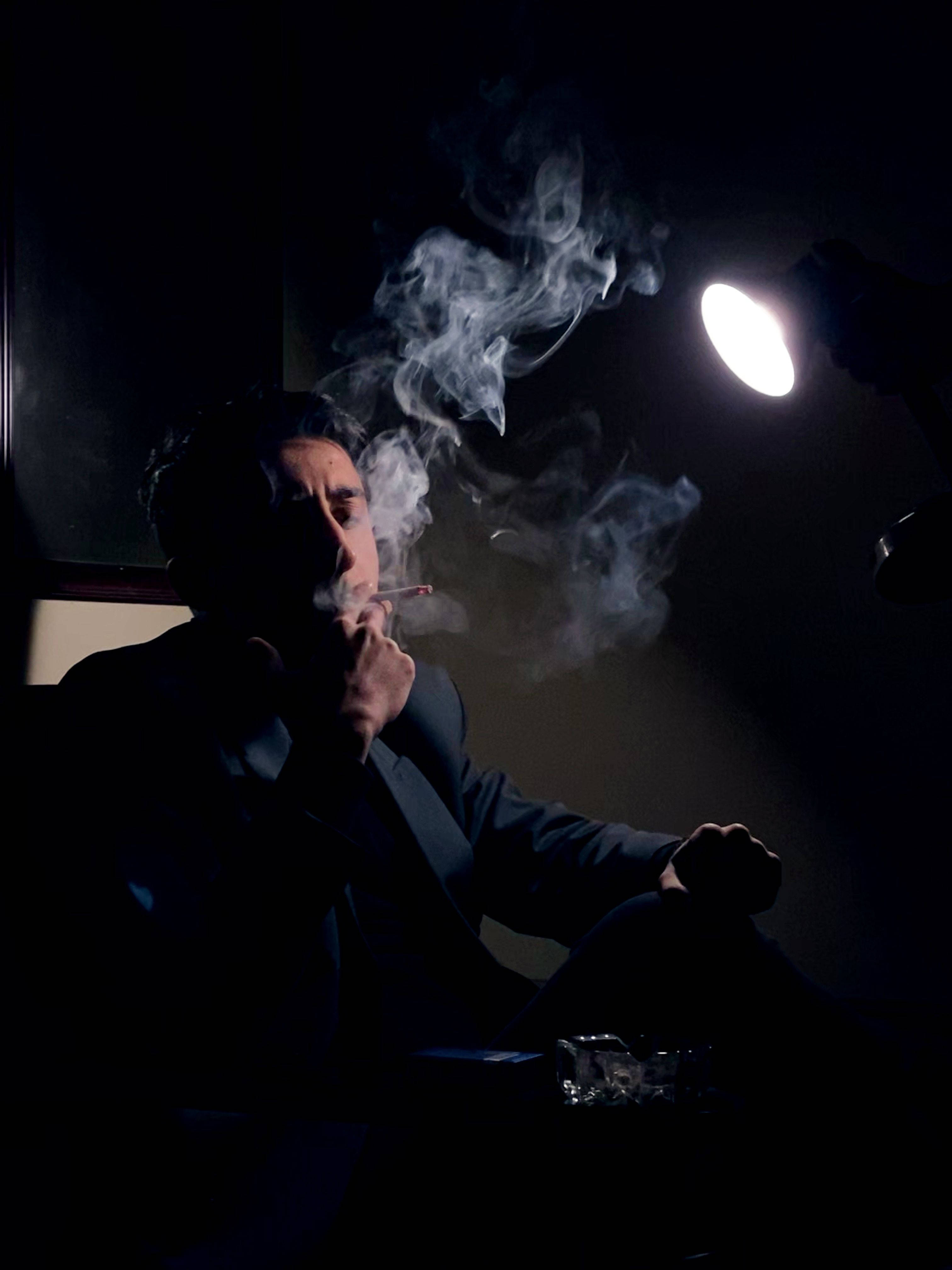 Man 桌布 壁紙 — 一個穿著西裝的男人在黑暗的房間裡，在單一明亮燈光下抽煙，煙霧繚繞。
