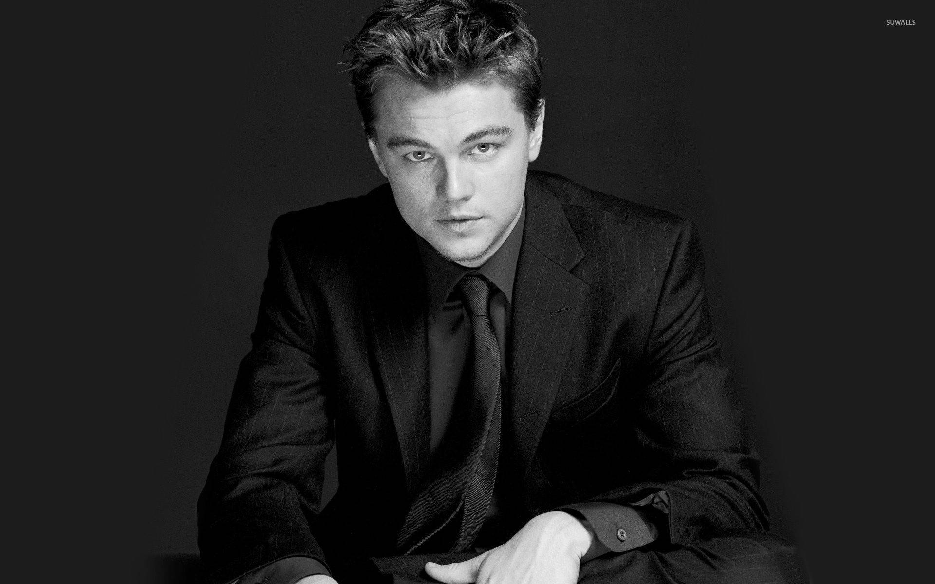 Dicaprio 桌布 壁紙 — 一個穿著西裝的男人在黑色背景下直視鏡頭，眼神銳利的黑白肖像。