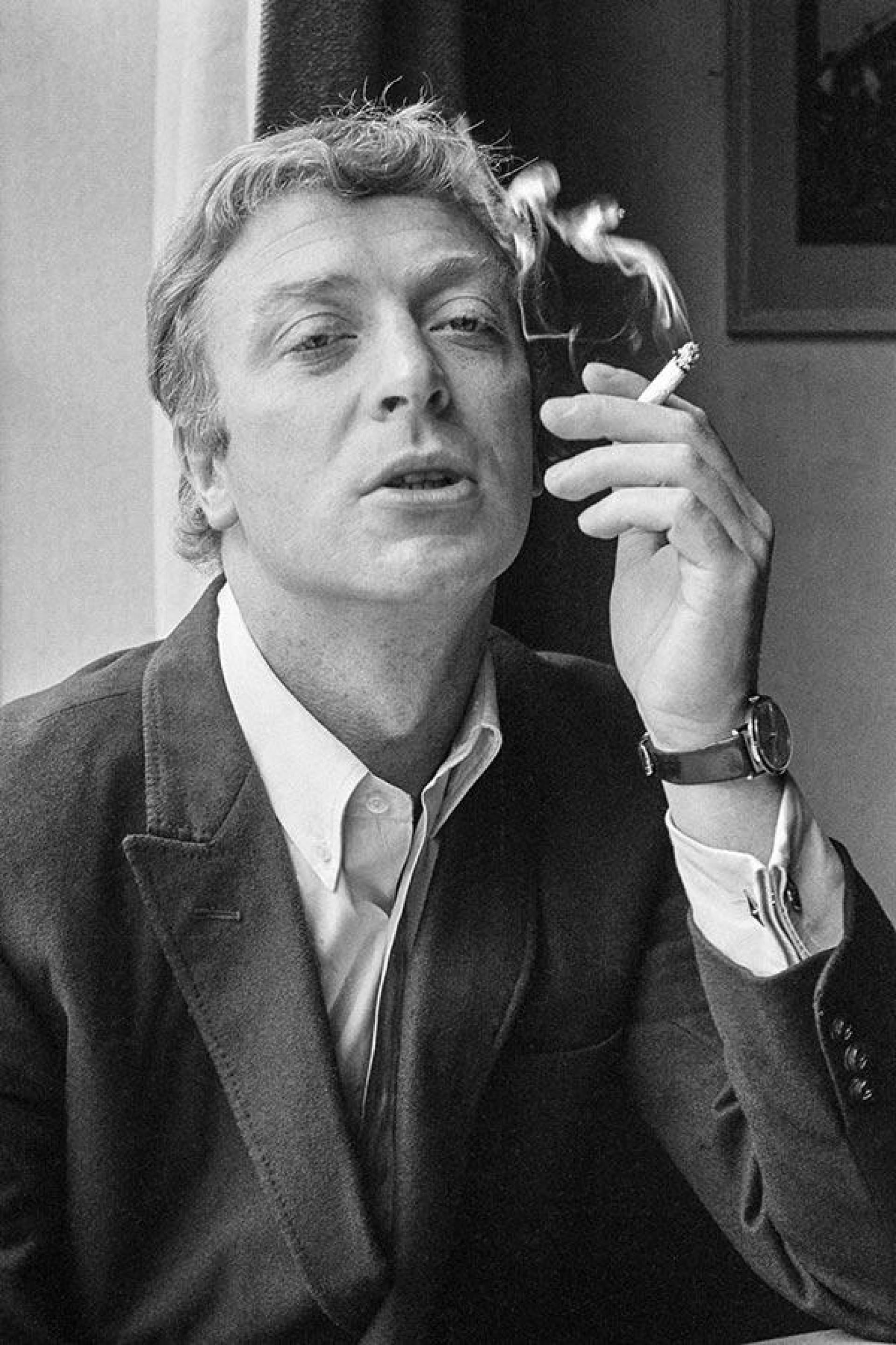 actor 桌布 壁紙 — 一個穿著西裝的男人手持香菸，煙霧在他臉旁向上繚繞的黑白肖像。