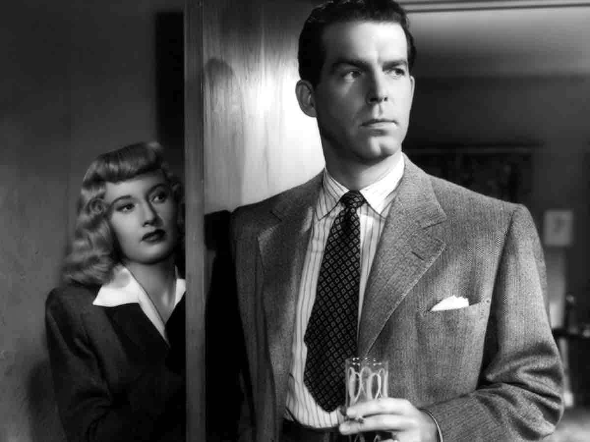Film Noir 桌布 壁紙 — 一個穿著西裝的男人拿著酒杯，站在一個從門後偷看的女人旁邊，經典黑色電影黑白場景。