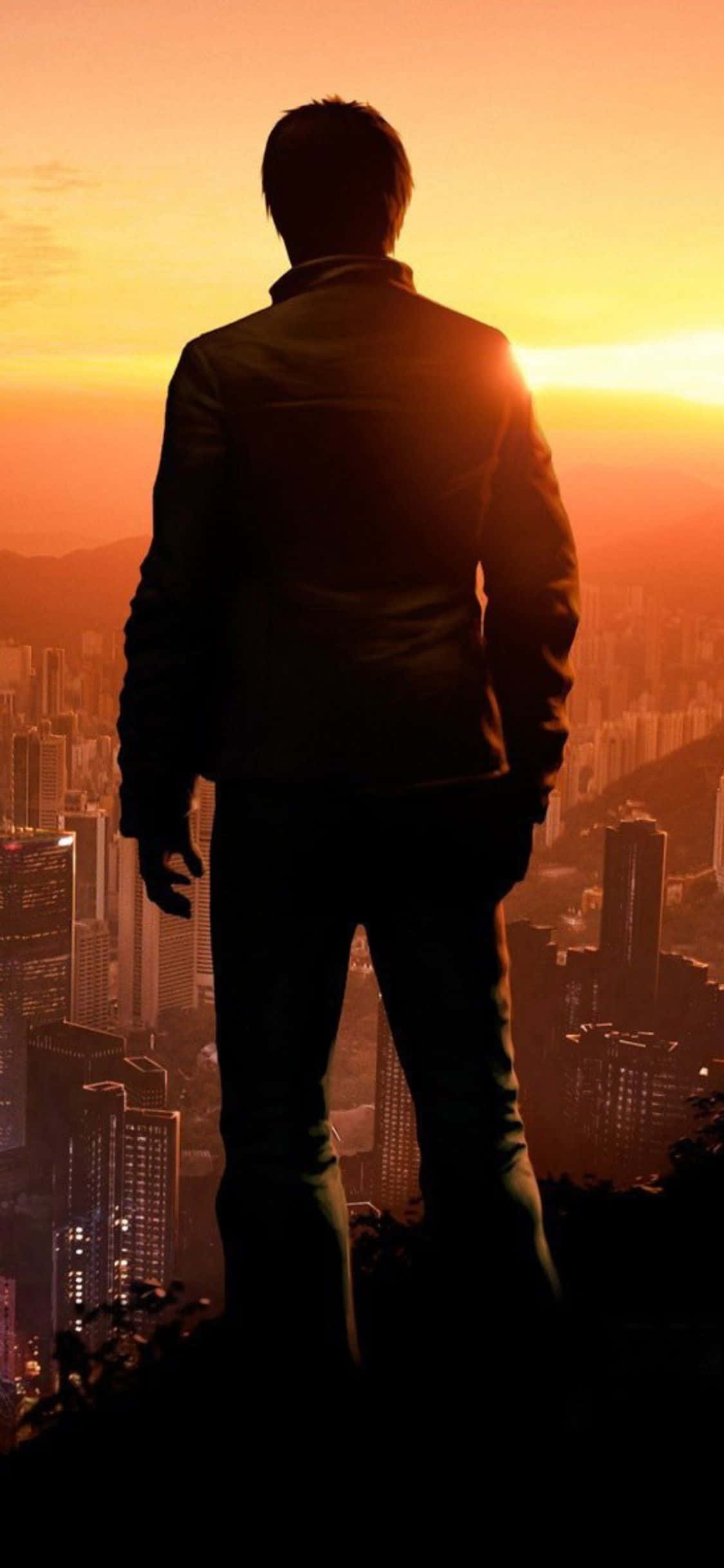City Sunset iPhone 桌布 壁紙 — 一個穿著西裝的男人的孤獨剪影站在山頂上，俯瞰著夕陽下溫暖橙色和黃色調的廣闊城市。