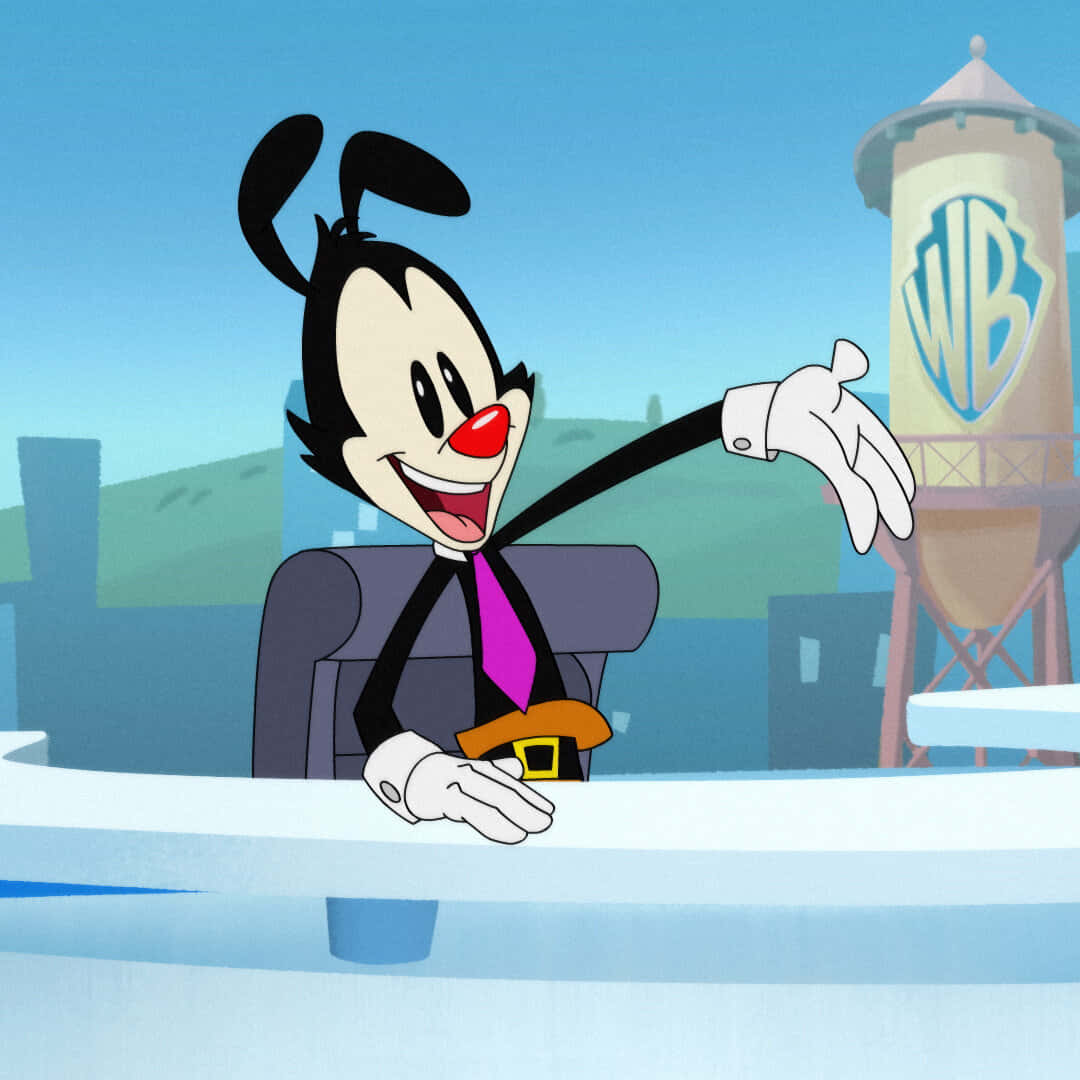 Animaniacs 桌布 壁紙 — 一個穿著西裝的開心卡通角色在辦公桌旁做手勢，背景是華納兄弟的水塔。