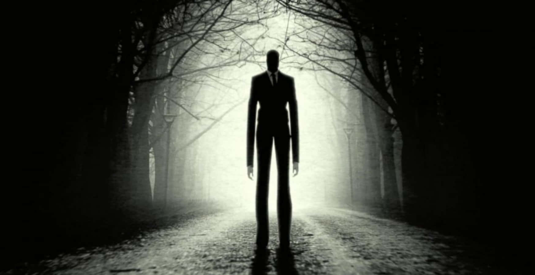 Creepypasta 桌布 壁紙 — 一個穿著西裝的高大沉默身影，站在一條霧氣瀰漫、兩旁樹木林立的小徑盡頭，沐浴在詭異的背光中。
