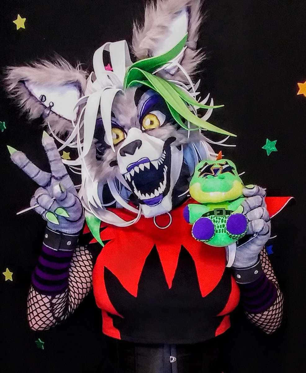 Roxanne Wolf 桌布 壁紙 — 一個穿著詳細狼人角色扮演服裝、有綠色頭髮和尖牙的人，在星空黑色背景前拿著毛絨玩具擺姿勢。