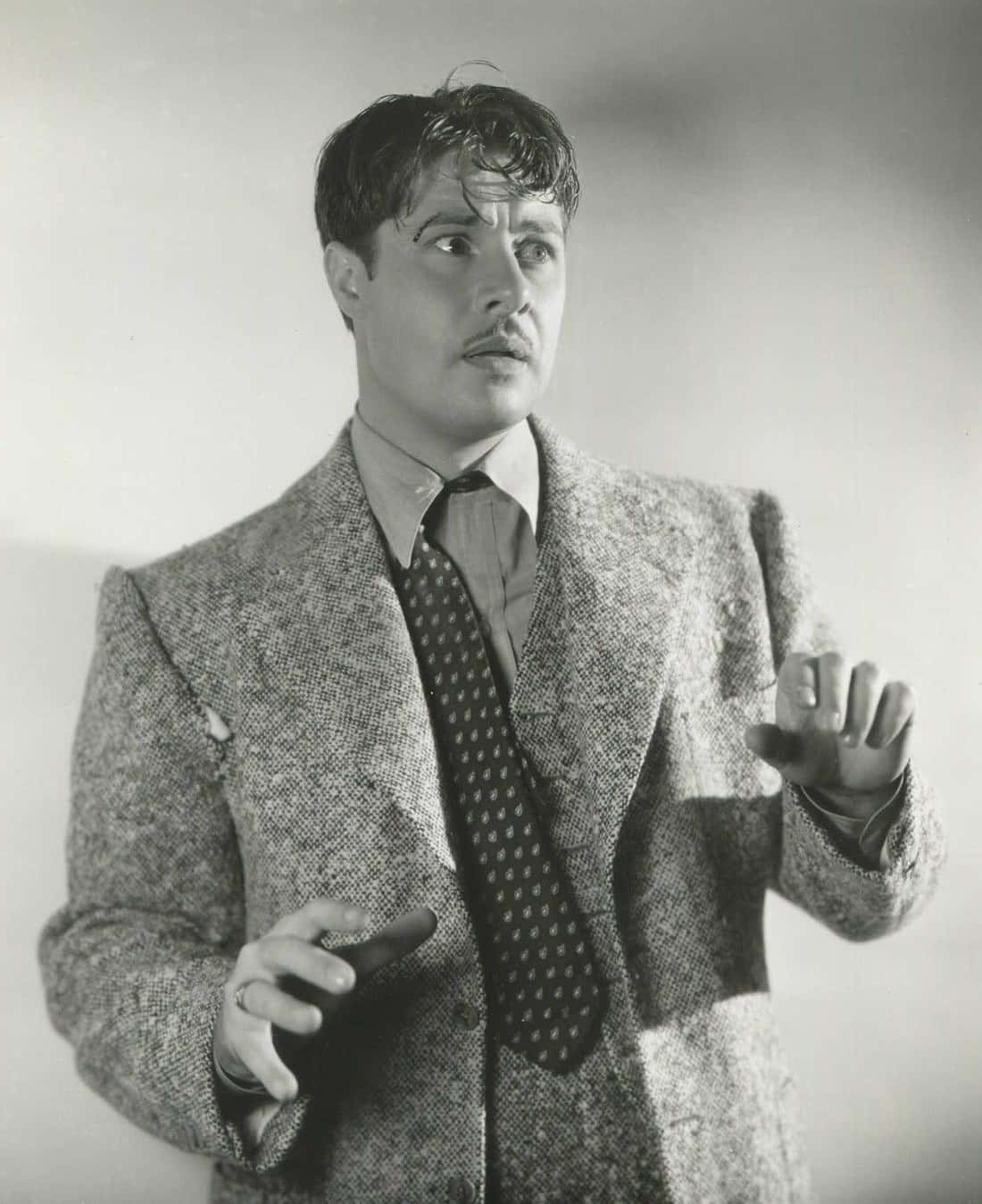 Don Ameche 桌布 壁紙 — 一個穿著質感西裝和圖案領帶的男人在純色工作室背景前富有表情地做手勢，復古黑白肖像。