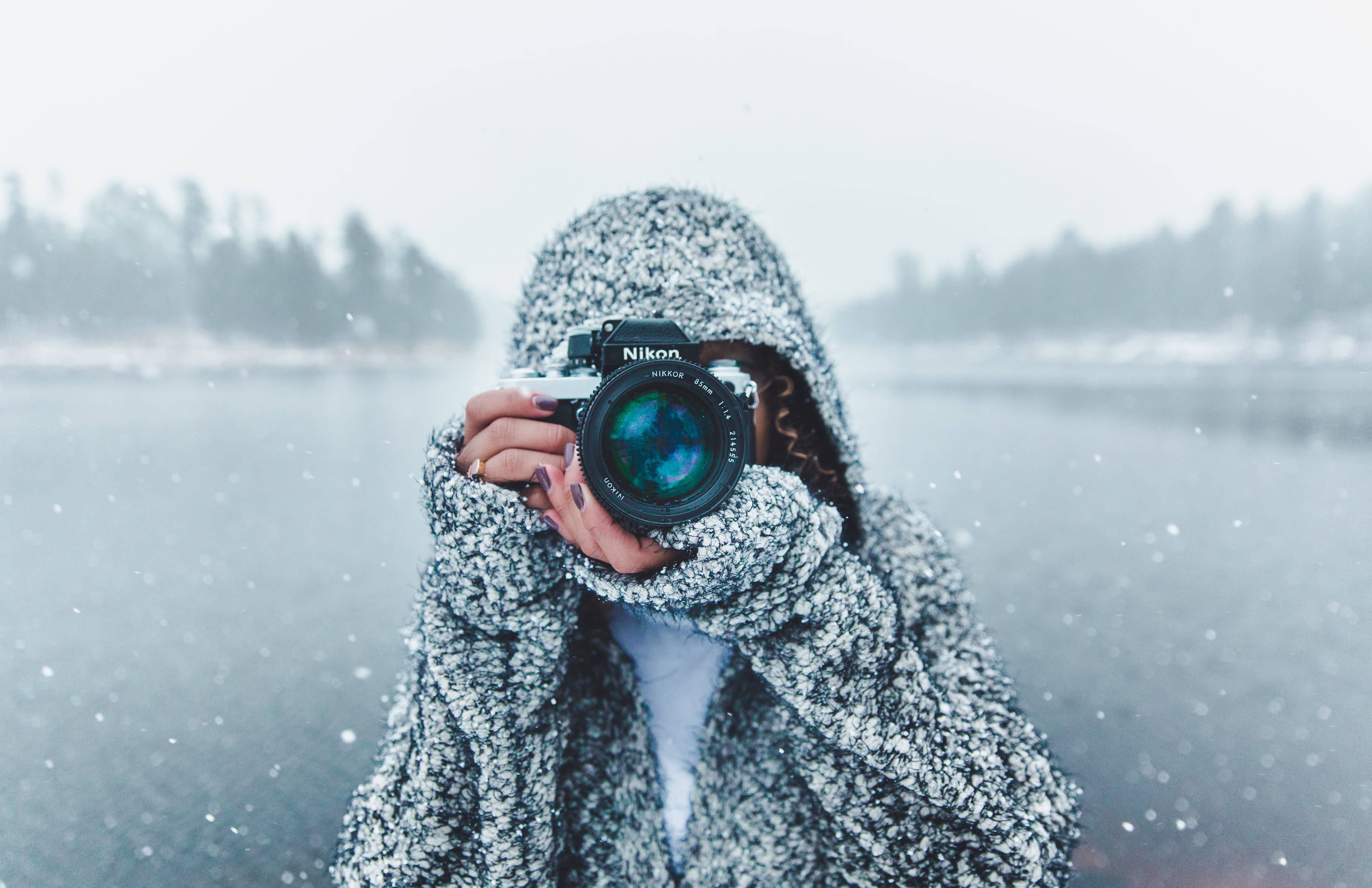 Temperature 桌布 壁紙 — 一個穿著質感連帽外套的人，在雪白模糊的冬季風景中將相機舉到臉前。