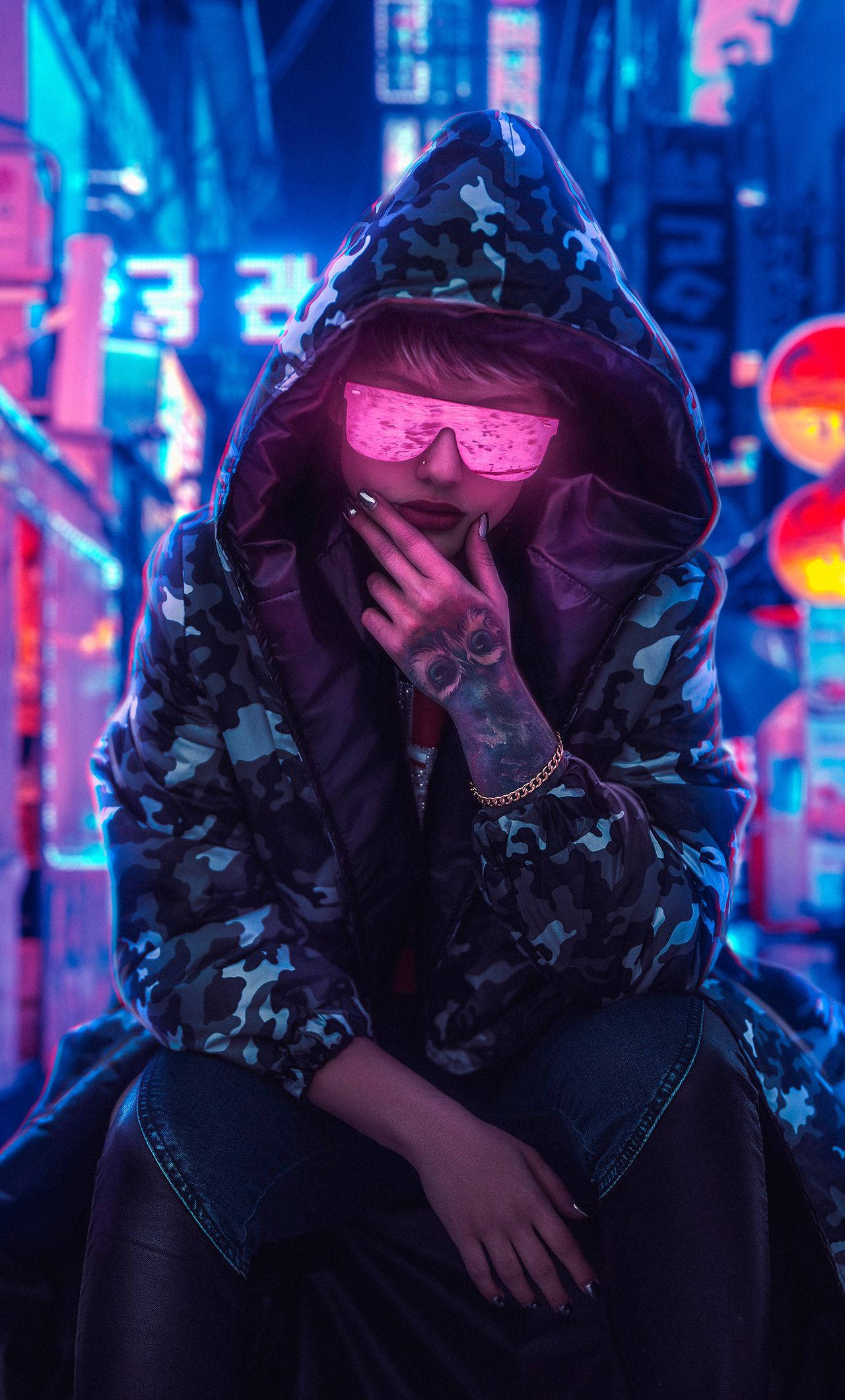 Hoodie 桌布 壁紙 — 一個穿著迷彩連帽衫和粉紅色發光太陽眼鏡的人坐在霓虹燈照亮的賽博朋克小巷中。