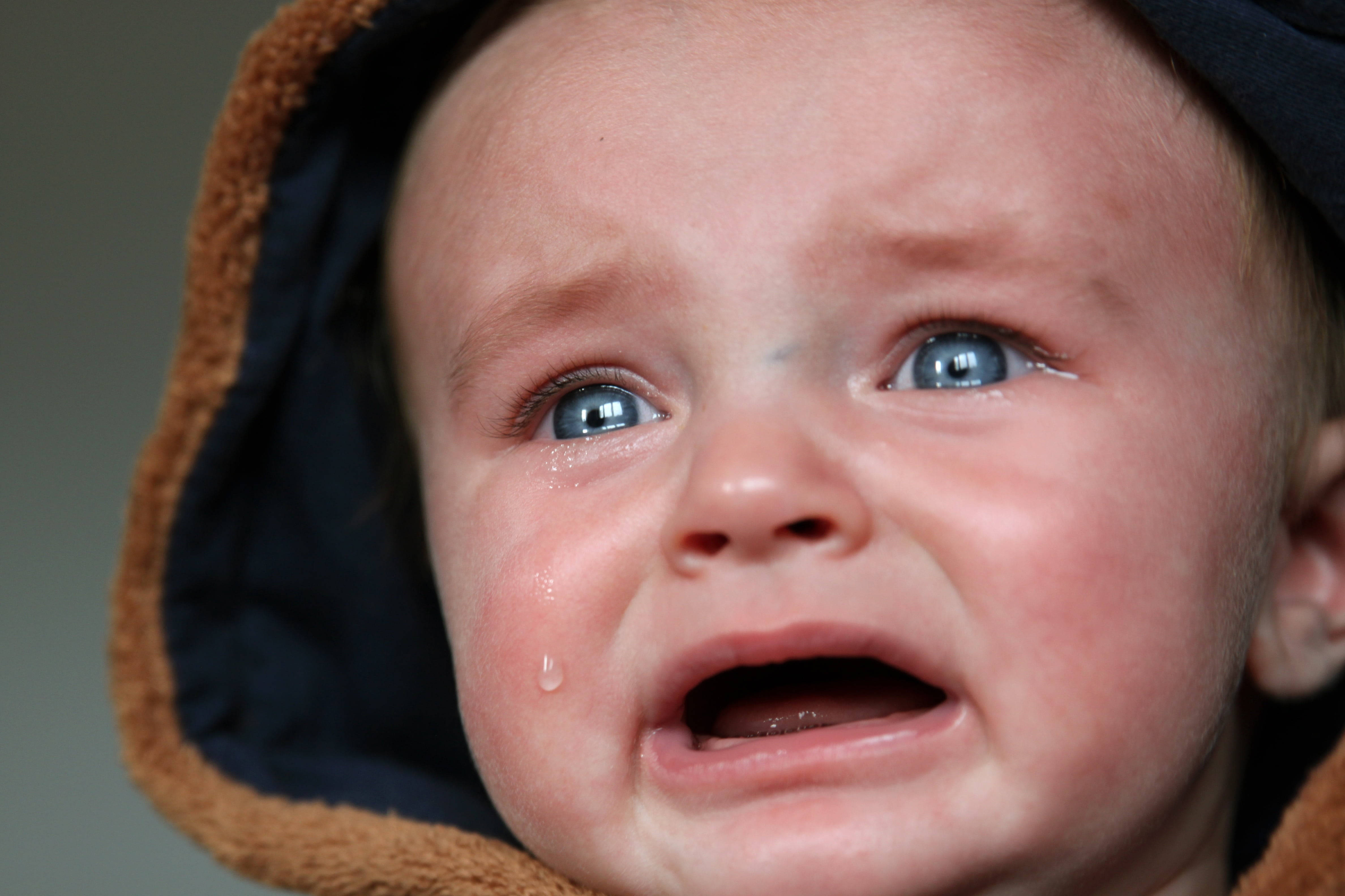crying sad boy 桌布 壁紙 — 一個穿著連帽外套、擁有明亮藍眼睛且淚水順著臉頰流下的哭泣嬰兒特寫。