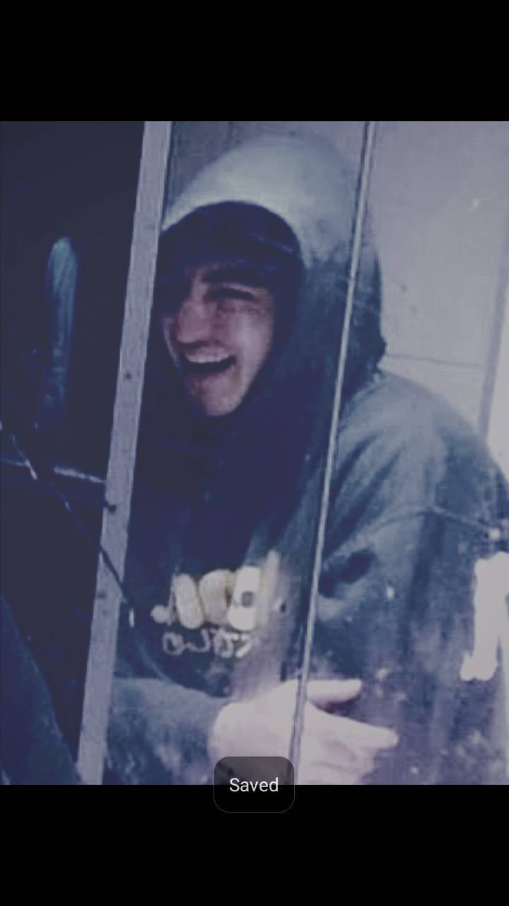 joji 桌布 壁紙 — 一個穿著連帽外套的人在一塊有明顯污漬和反射的玻璃後面開心地笑。