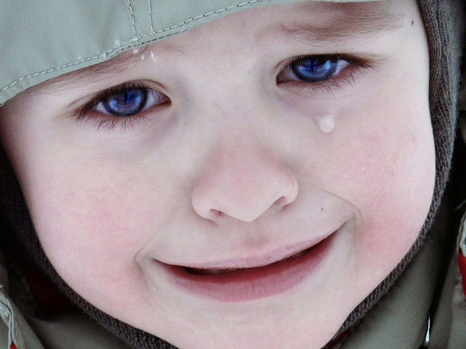cry 桌布 壁紙 — 一個穿著連帽外套的孩子，擁有引人注目的藍色眼睛，微笑著，淚水順著臉頰流下。