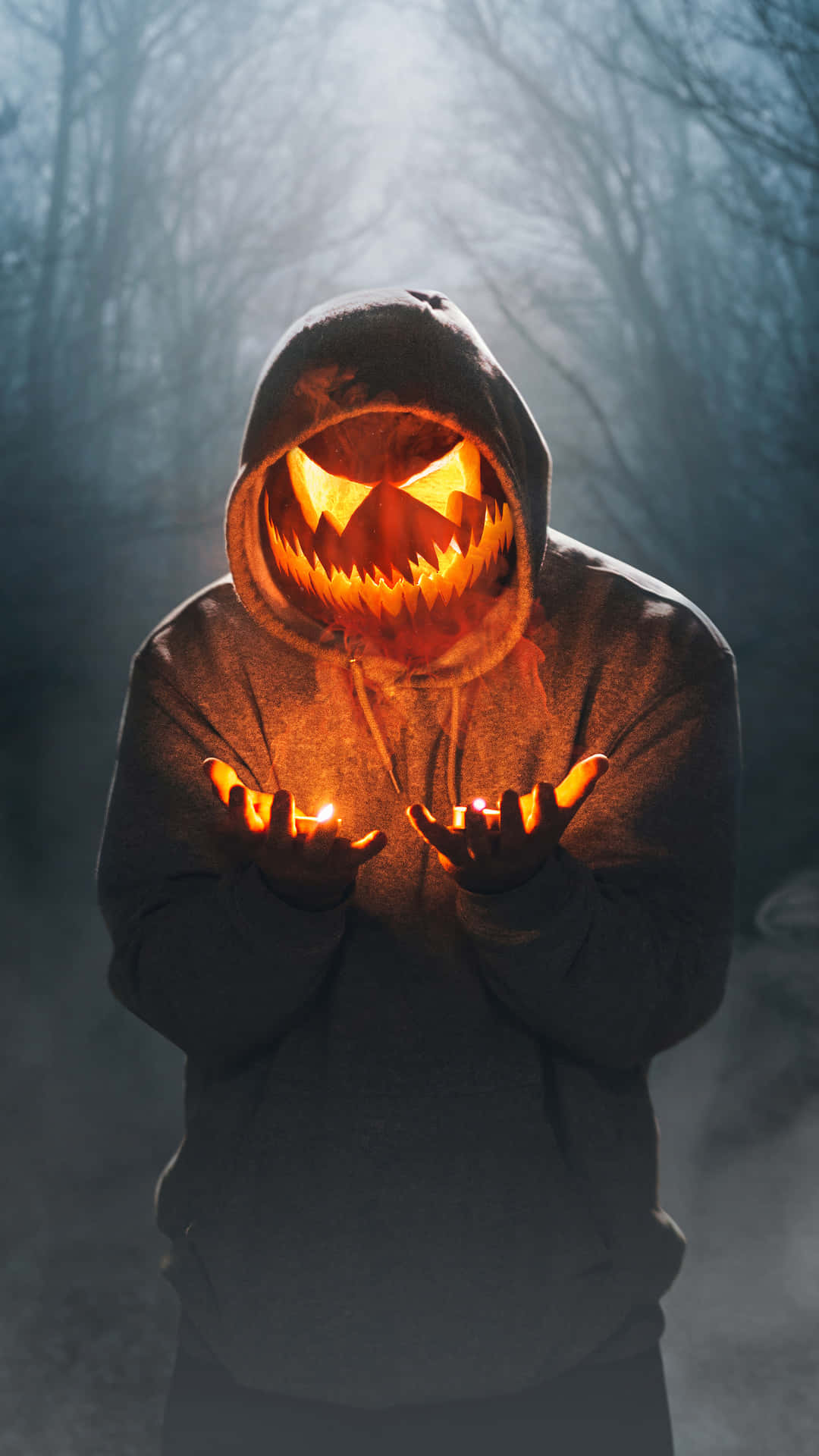 Mask Boy 桌布 壁紙 — 一個穿著連帽衫、有著發光南瓜臉的人站在迷霧森林中手持蠟燭。