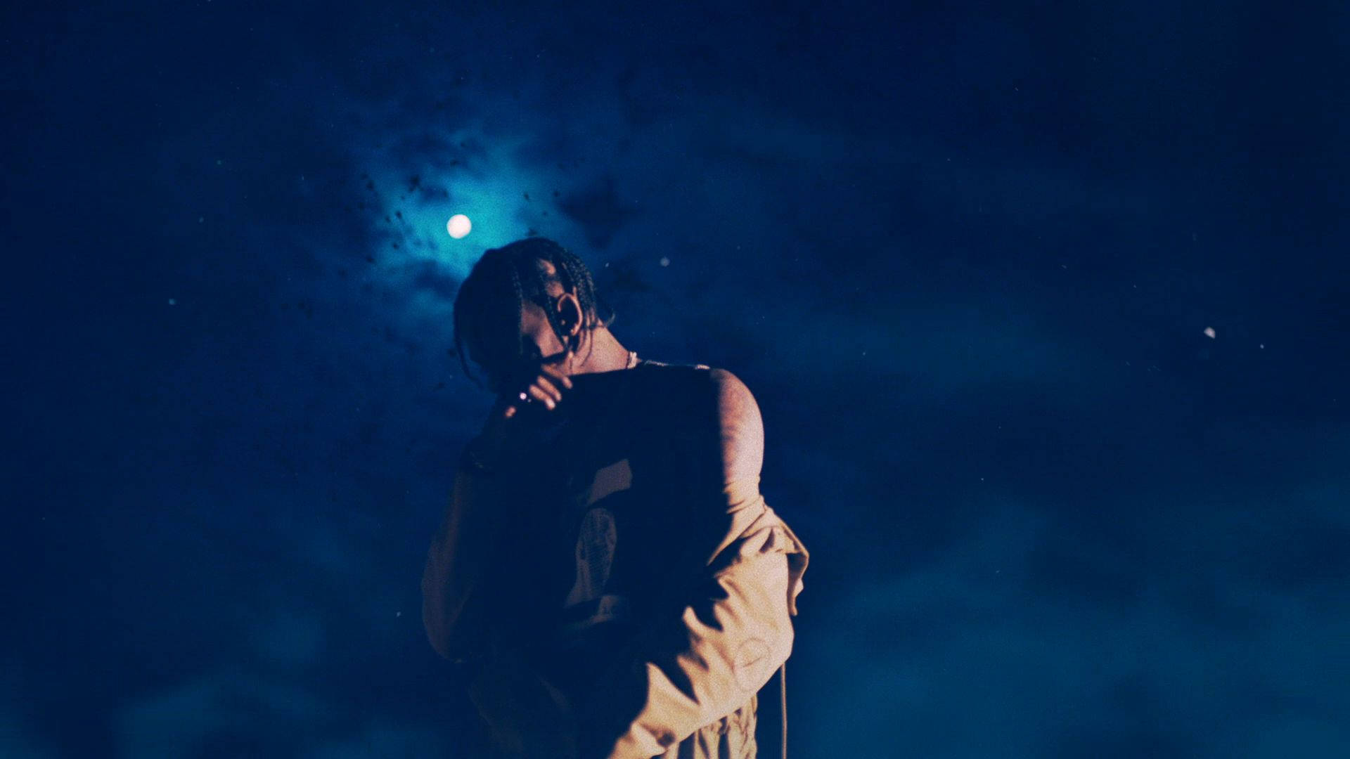 Astroworld 桌布 壁紙 — 一個穿著連帽衫的人站在深藍色夜空下，背景有發光的月亮和微弱的星星，形成剪影。