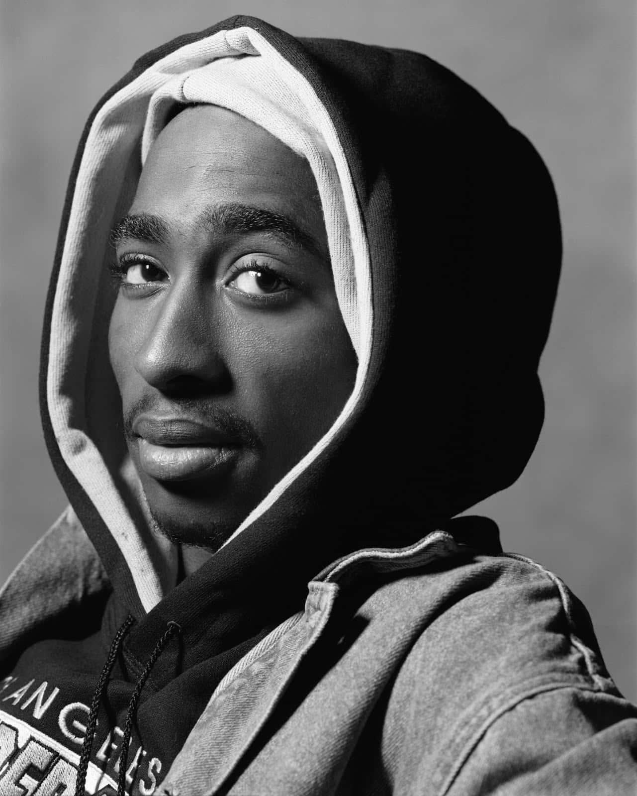 一個穿著連帽衫的男人在黑白工作室肖像中直視鏡頭。 — Tupac GIF 壁紙