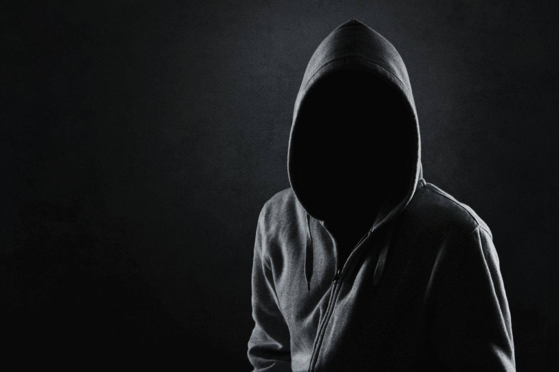 Hood 桌布 壁紙 — 一個穿著連帽衫的神秘身影站在黑暗背景前，臉部被深沉的陰影遮蓋。