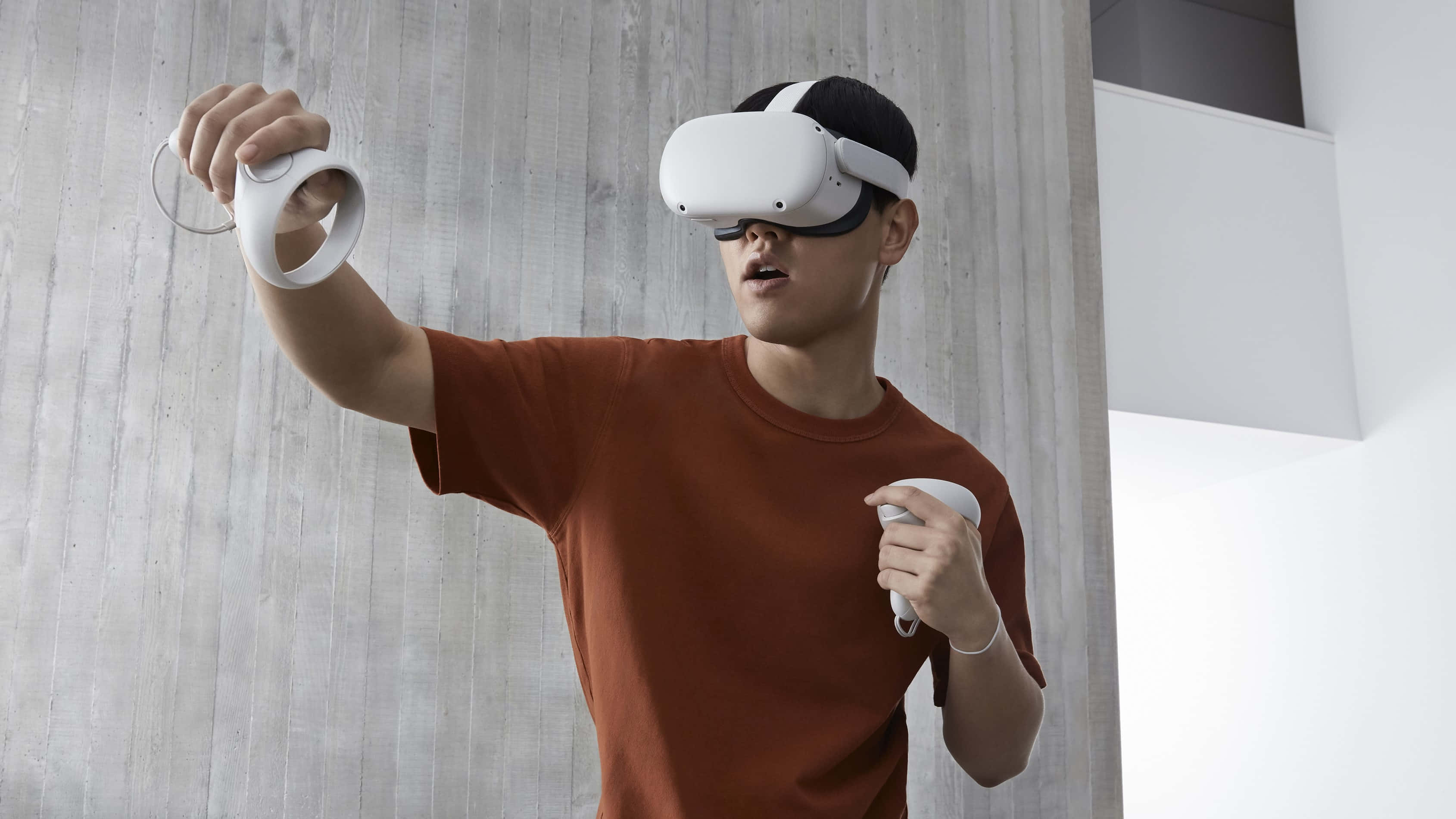 Oculus Quest 2 桌布 壁紙 — 一個穿著鏽色襯衫的人，戴著白色頭戴式顯示器和控制器，沉浸在虛擬現實中，背景是混凝土牆。