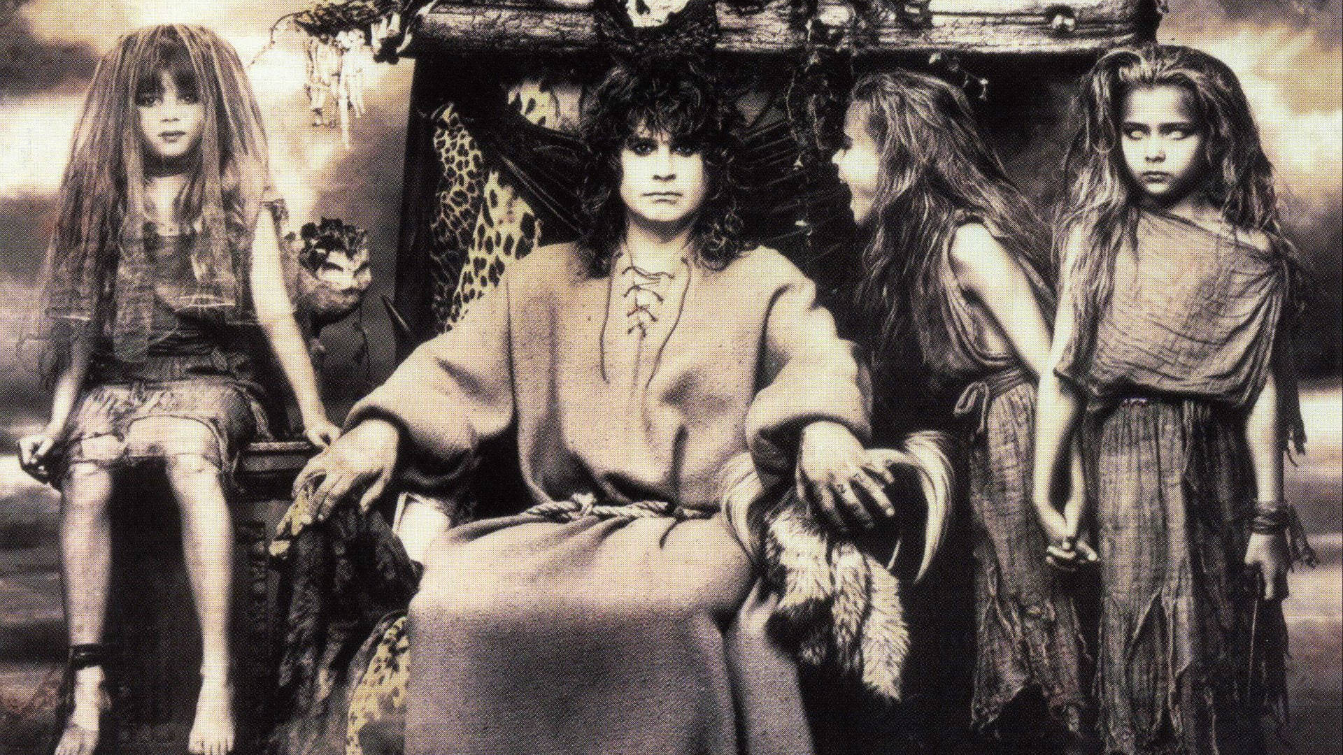 Ozzy Osbourne 桌布 壁紙 — 一個穿著長袍的男人威嚴地坐在王座上，兩旁有三個年輕女孩，場景是棕褐色調的奇幻場景。