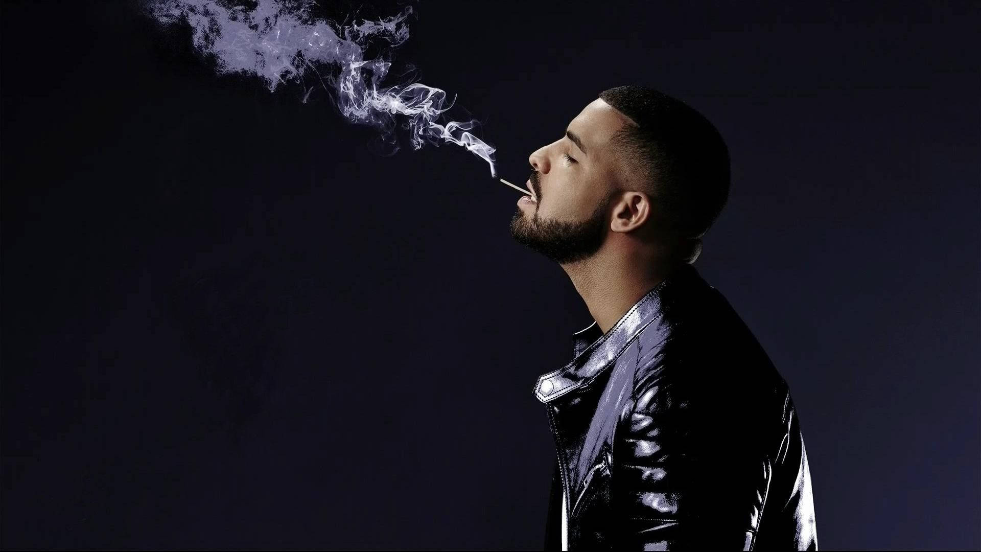 Drake 桌布 壁紙 — 一個穿著閃亮黑色外套的男人在黑暗背景下呼出一團旋轉的煙霧。