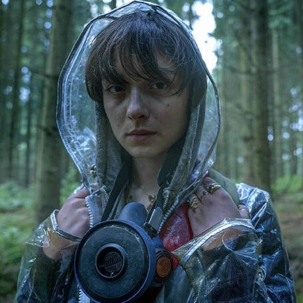 Netflix 桌布 壁紙 — 一個穿著雨衣和防毒面具的人，莊嚴地站在霧氣瀰漫的森林中，樹木高聳，光線柔和帶綠。