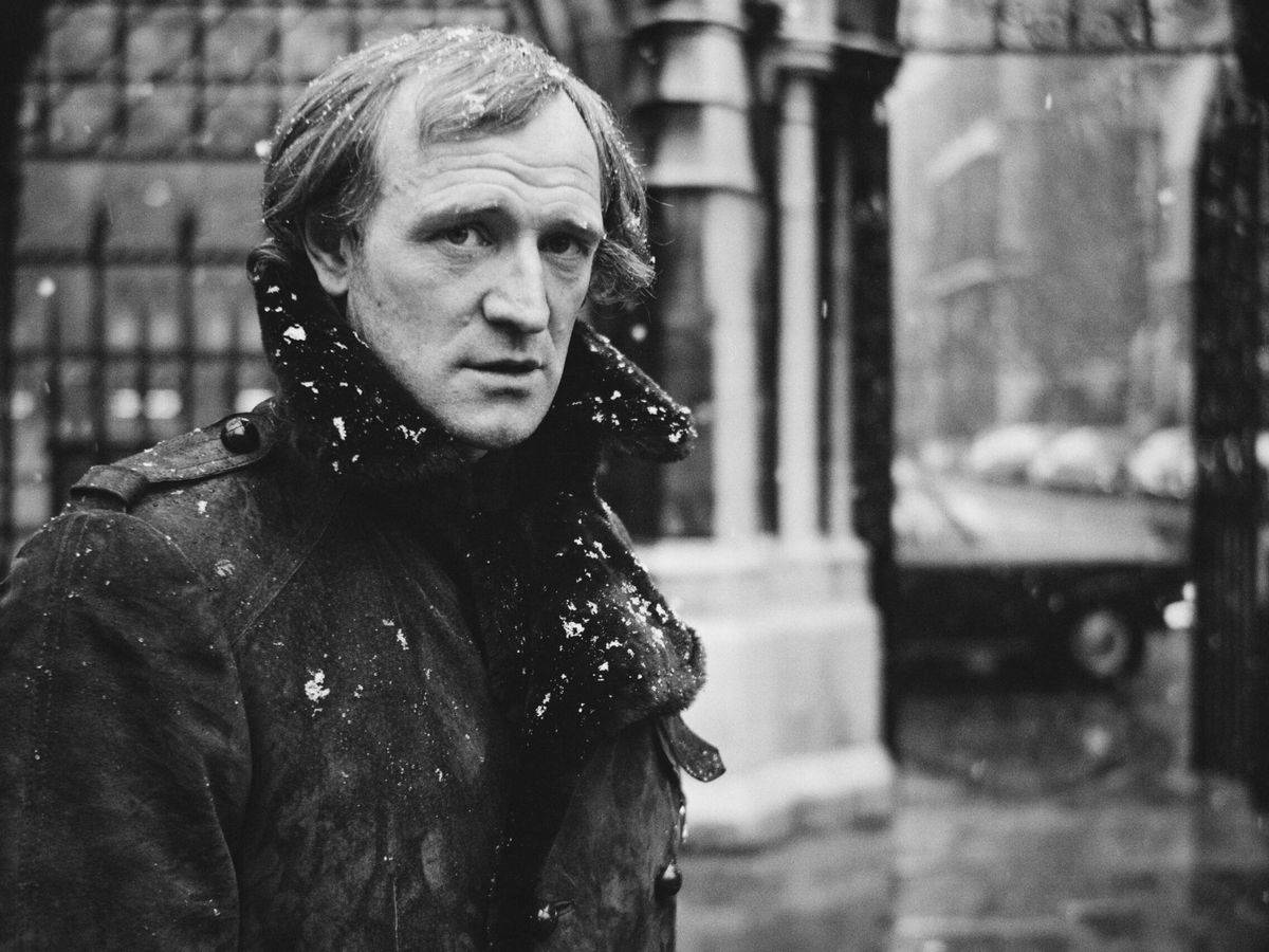 actor 桌布 壁紙 — 一個穿著雪外套的男人站在冬日城市街道上，雪花在他周圍飄落。