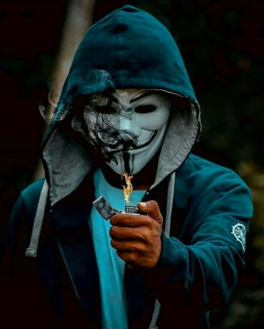 Cool Profile 桌布 壁紙 — 一個穿著青綠色連帽衫和蓋伊·福克斯面具的人，手持打火機，火焰向上舔舐，背景黑暗模糊。