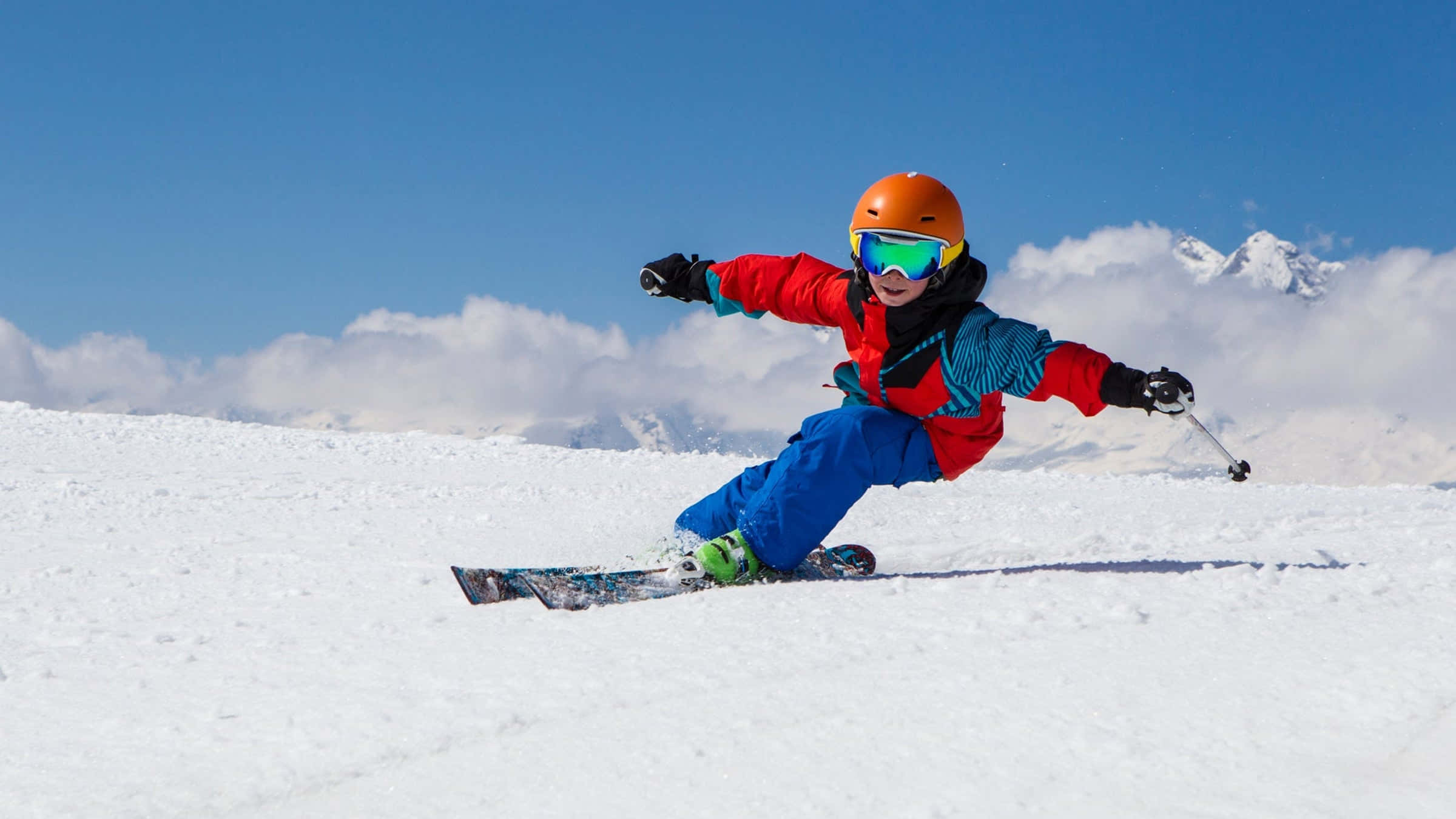 ski 桌布 壁紙 — 一個穿著鮮豔滑雪裝備的孩子在陽光明媚的山坡上穿過新雪，背景是白雪覆蓋的山峰。