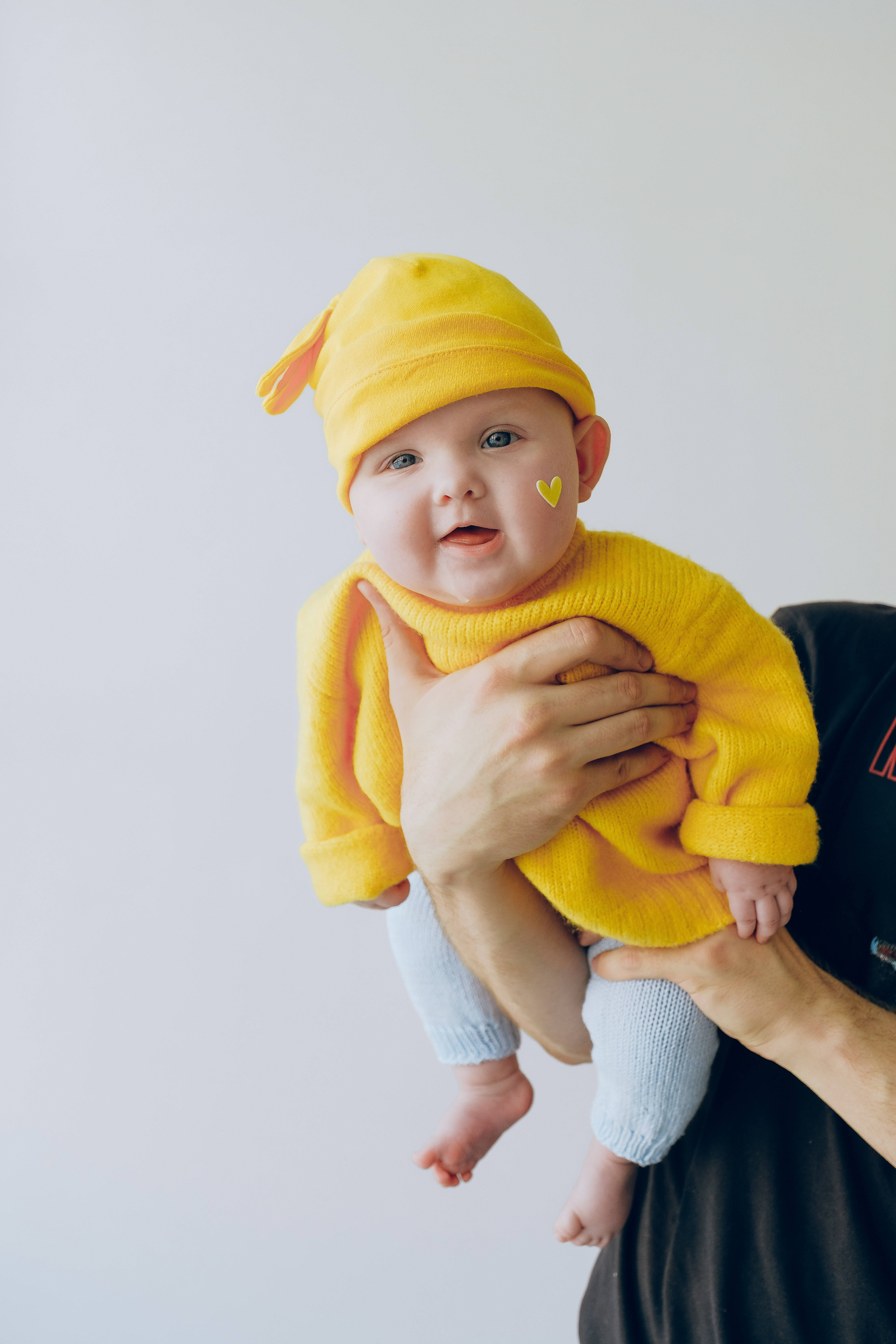 Smile 桌布 壁紙 — 一個穿著鮮黃色針織套裝和帽子的嬰兒，被一位成年人輕輕抱著，背景是純白色。