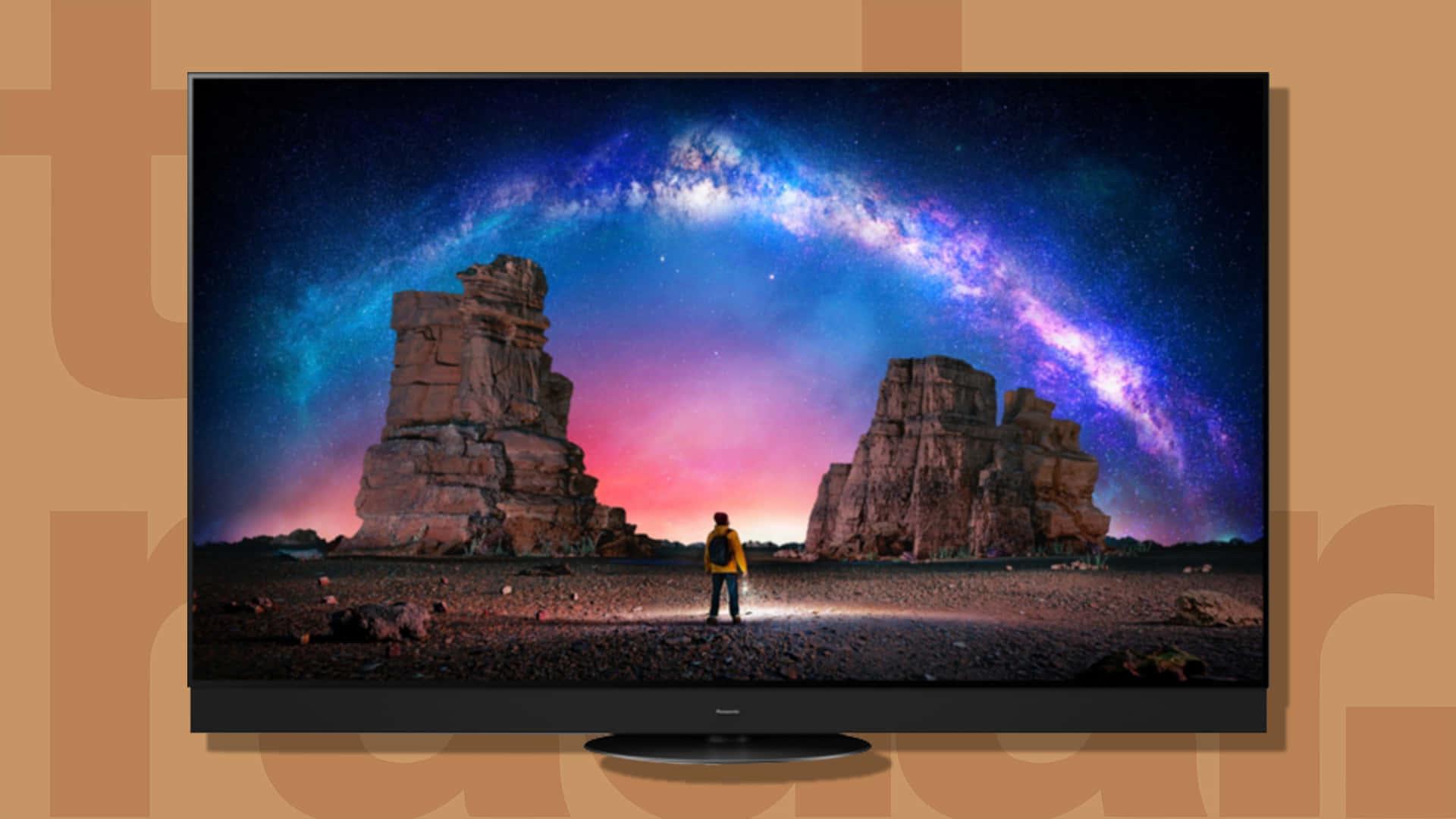 tv 桌布 壁紙 — 一個穿著黃色外套的孤獨身影，聳立在紫色和粉紅色銀河系下的高聳岩石之間。