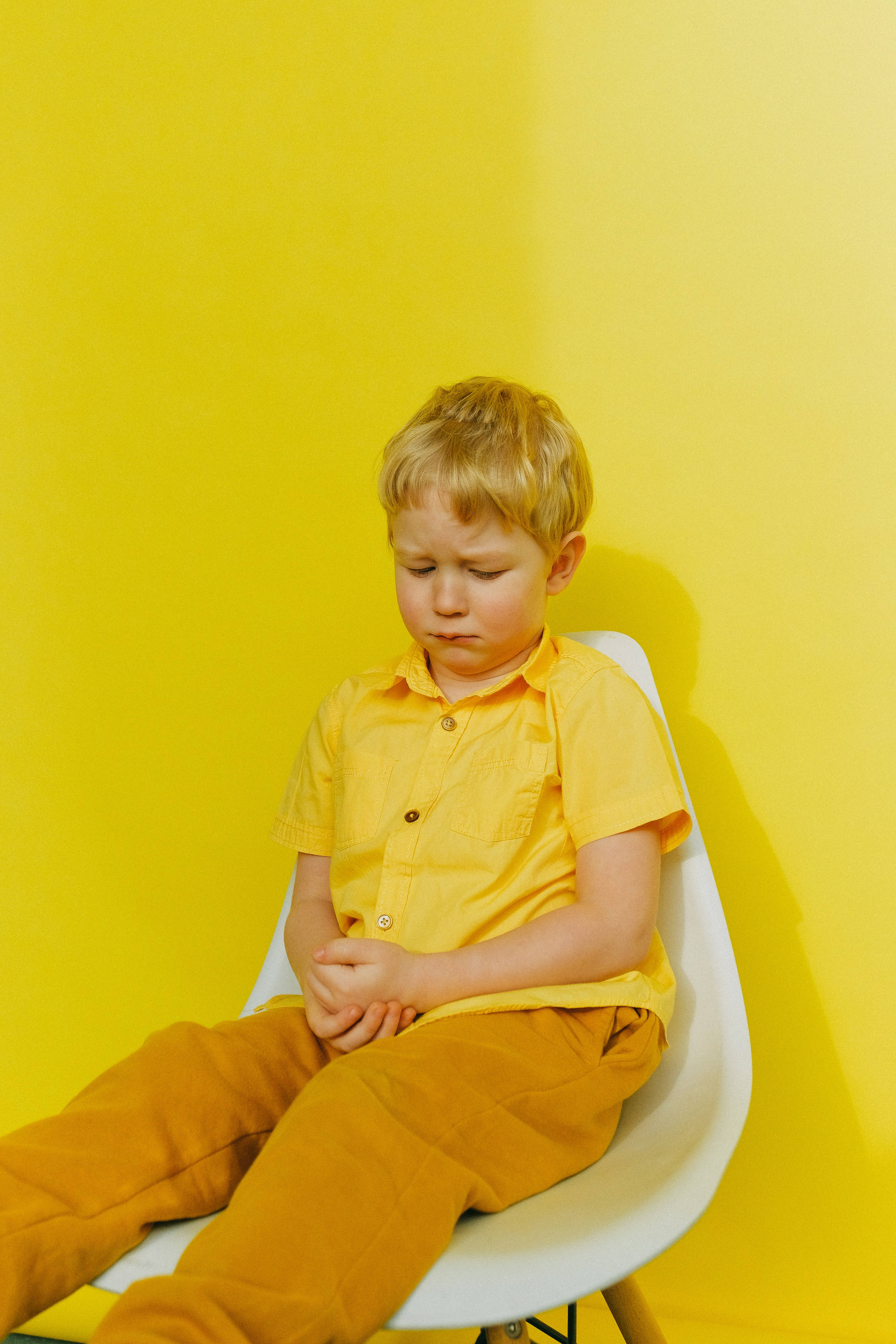 crying sad boy 桌布 壁紙 — 一個穿著黃色衣服的小男孩癱坐在白色椅子上，背景是鮮黃色的牆壁，看起來疲倦或悲傷。